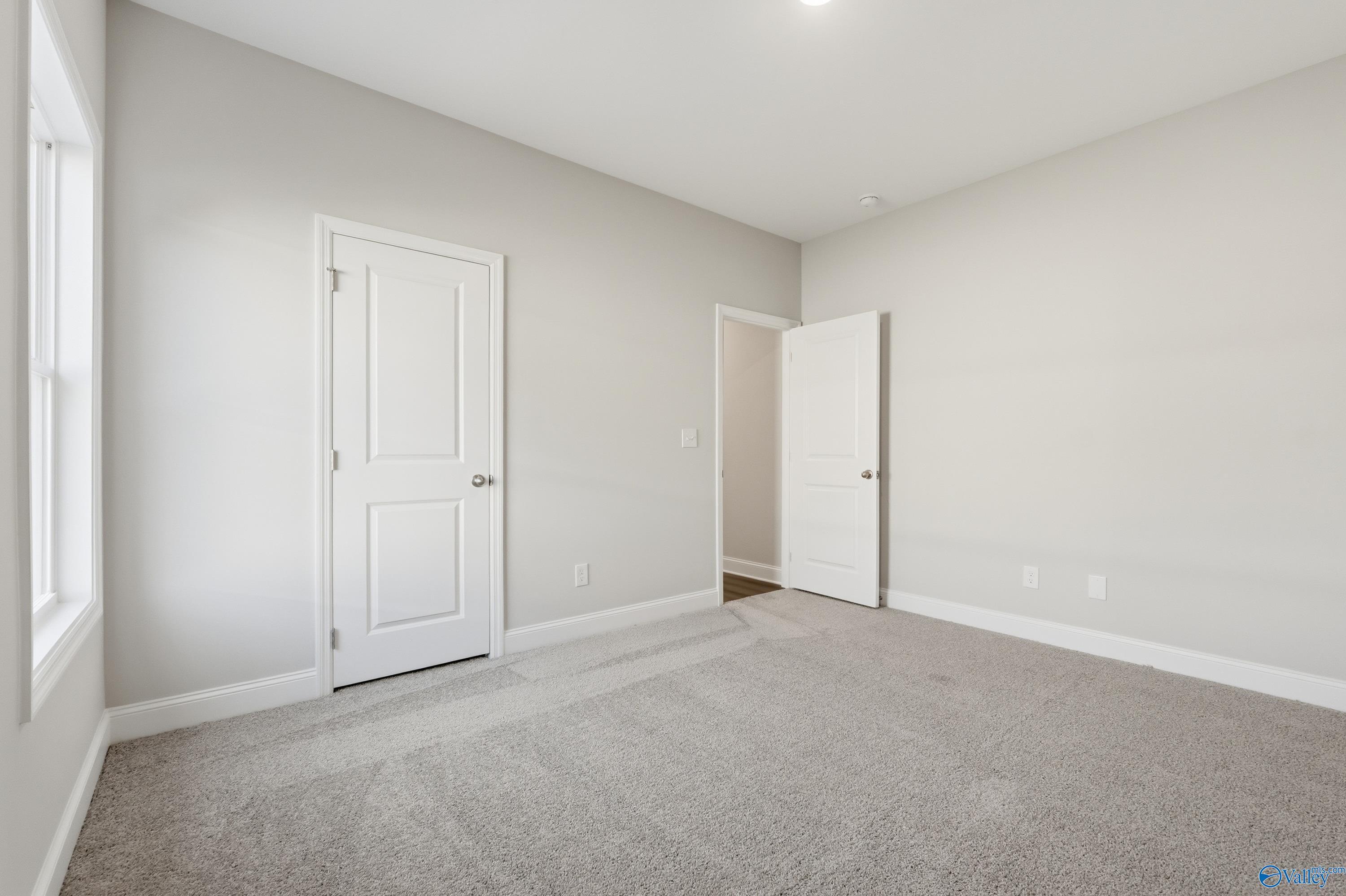Bright secondary bedroom with neutral gray walls, plush carpet, and adjacent bath door in Davidson Homes The Daphne C, Arab, Alabama