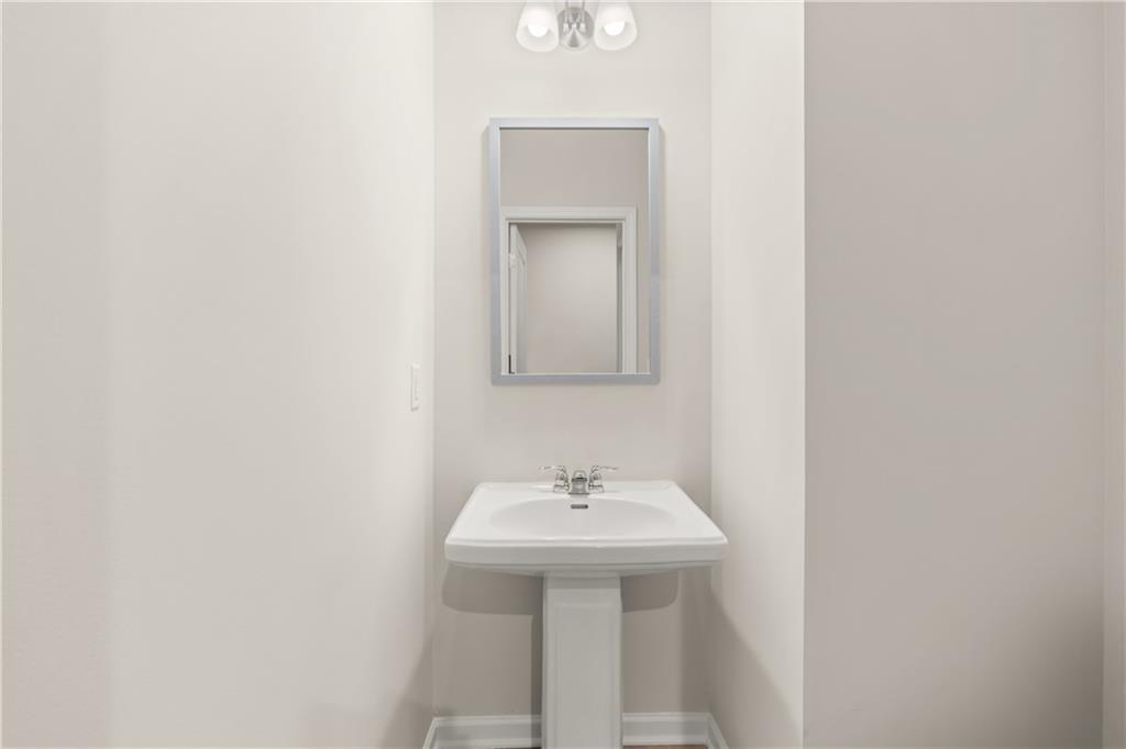 Bright powder room with white pedestal sink, framed mirror, and sconce lighting in Davidson Homes The Marion B, Kennesaw, Georgia