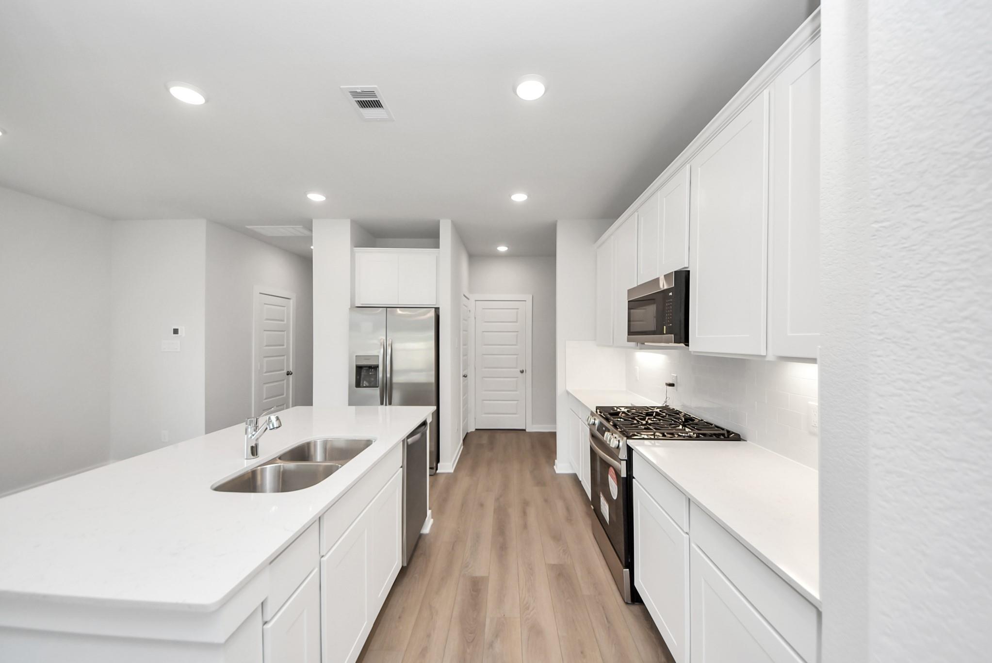 Modern kitchen with white cabinets, island, and stainless appliances in The Blanco E floor plan at The Villages, Dayton.