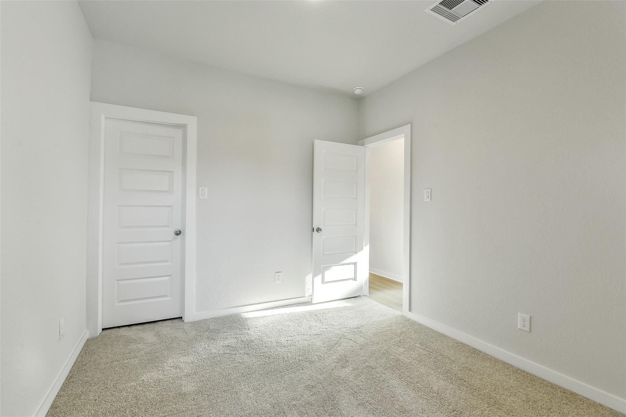 Bright empty secondary bedroom with beige carpet, neutral walls, and white doors in Davidson Homes The Colorado F, Cleveland, Texas
