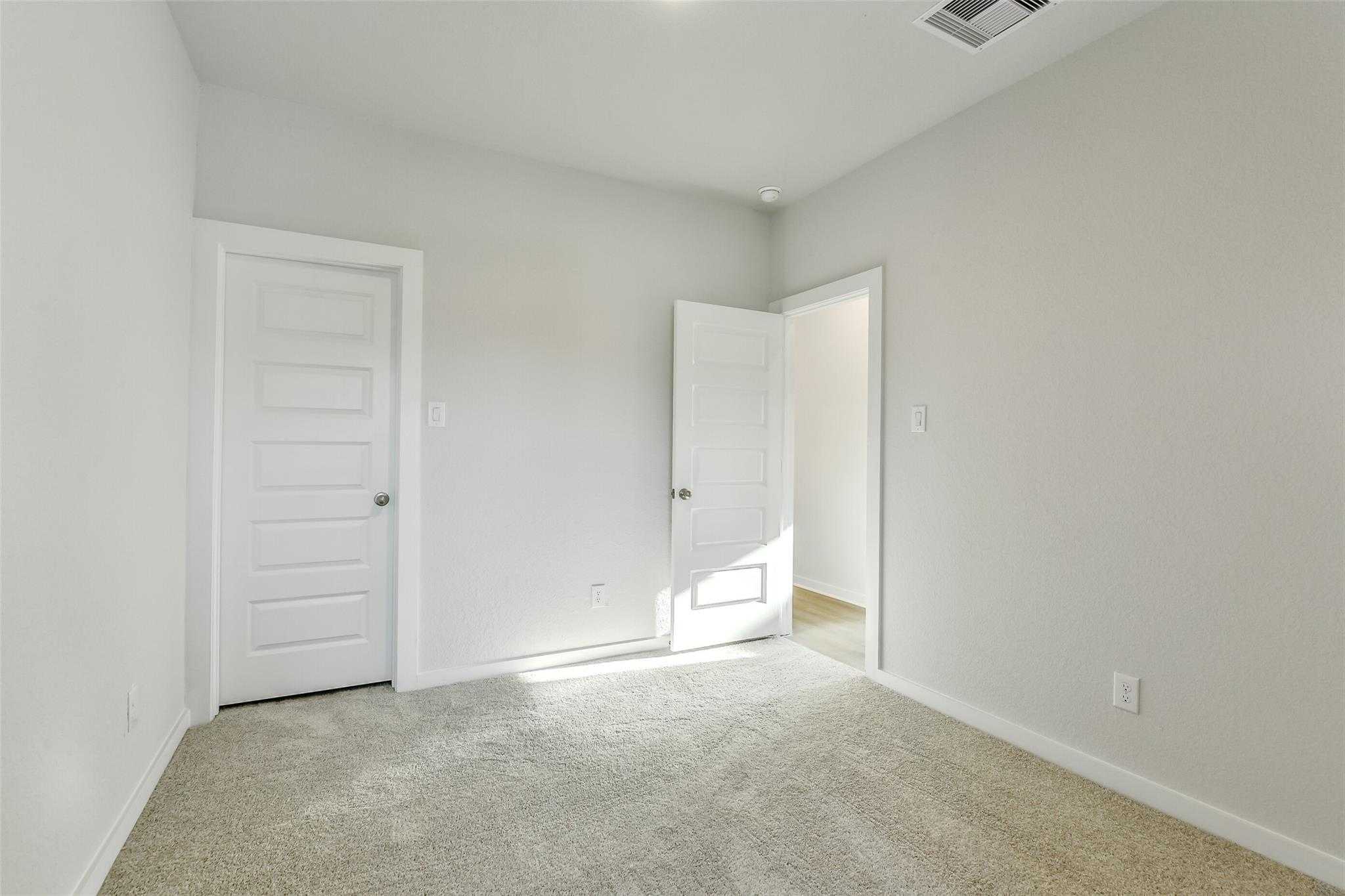 Bright secondary bedroom with light gray walls, beige carpet, and white doors in Davidson Homes The Colorado F, Cleveland, Texas