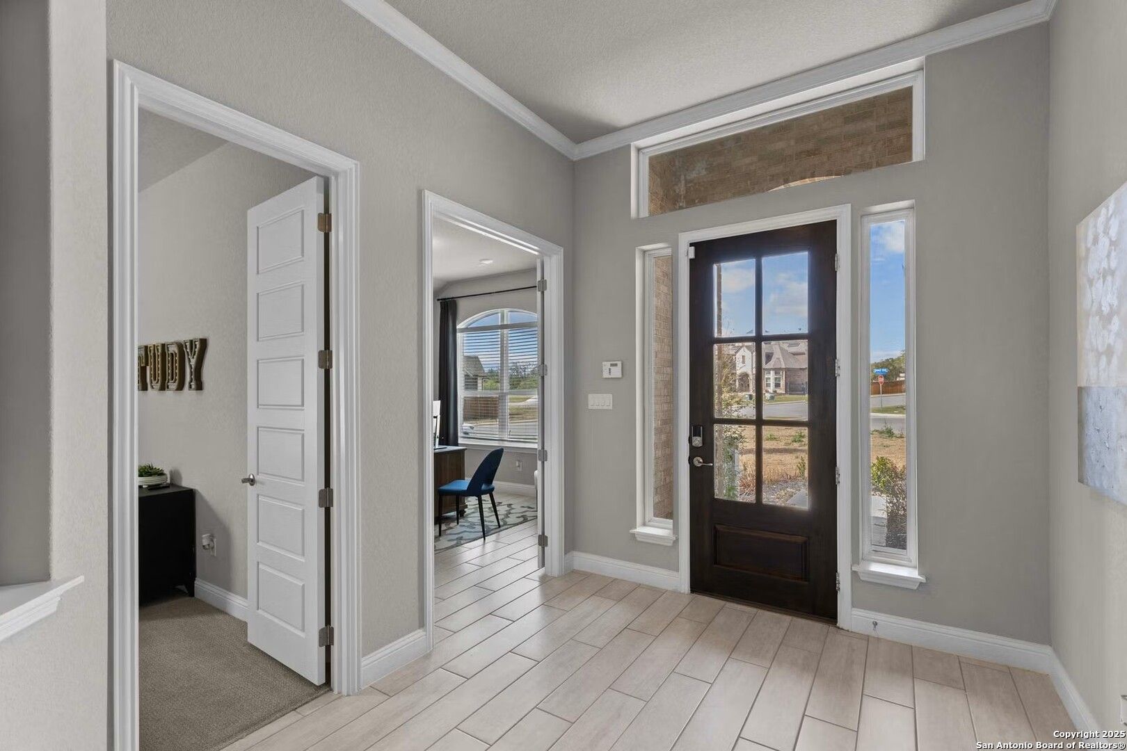 Spacious entryway with study view, dark wood front door, large windows, and tile floor in The Garner A, Castroville, Texas