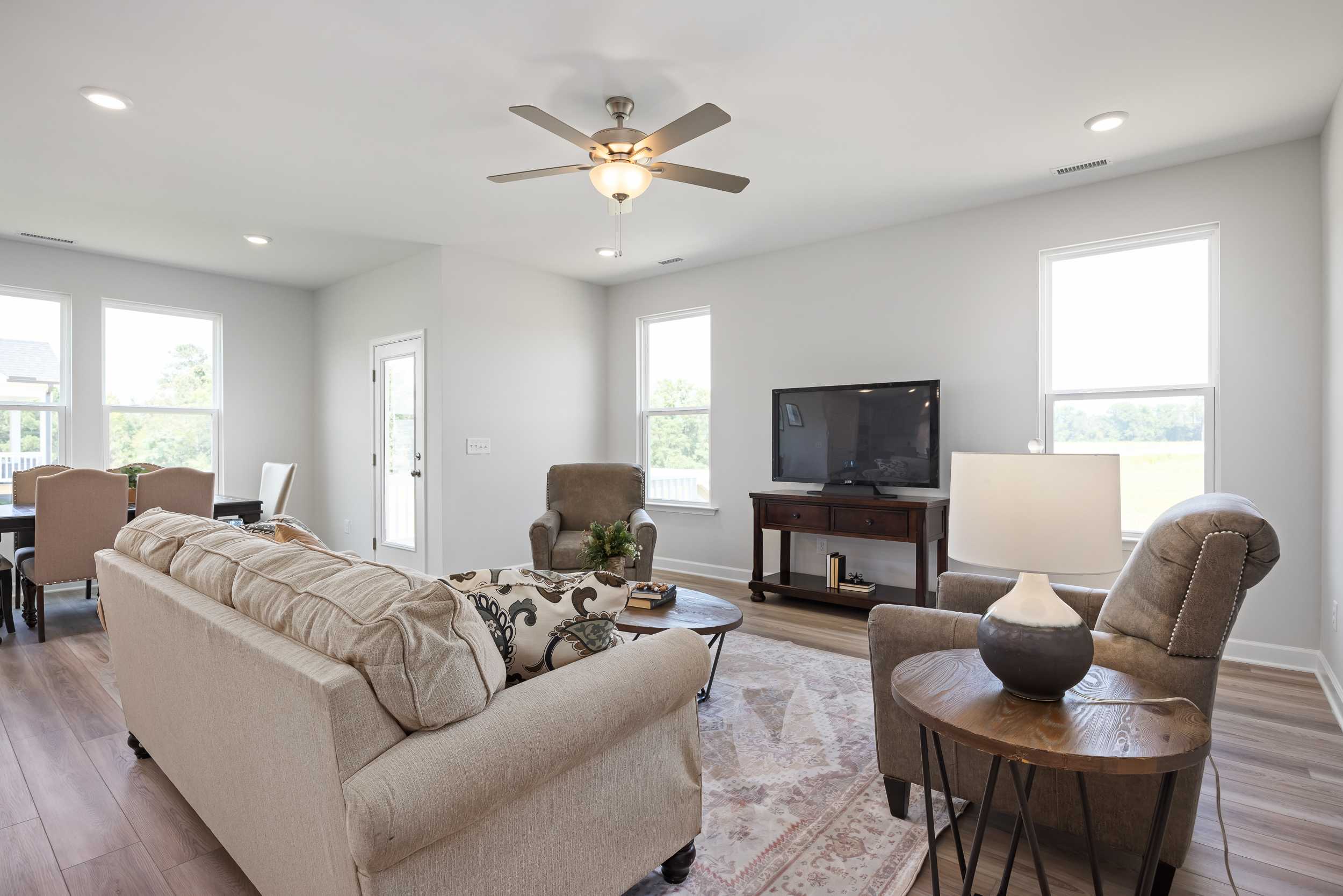 Spacious open-concept living room in The Daphne C by Davidson Homes, Mooresville NC: beige sofa, armchairs, TV console, ceiling fan, dining nook