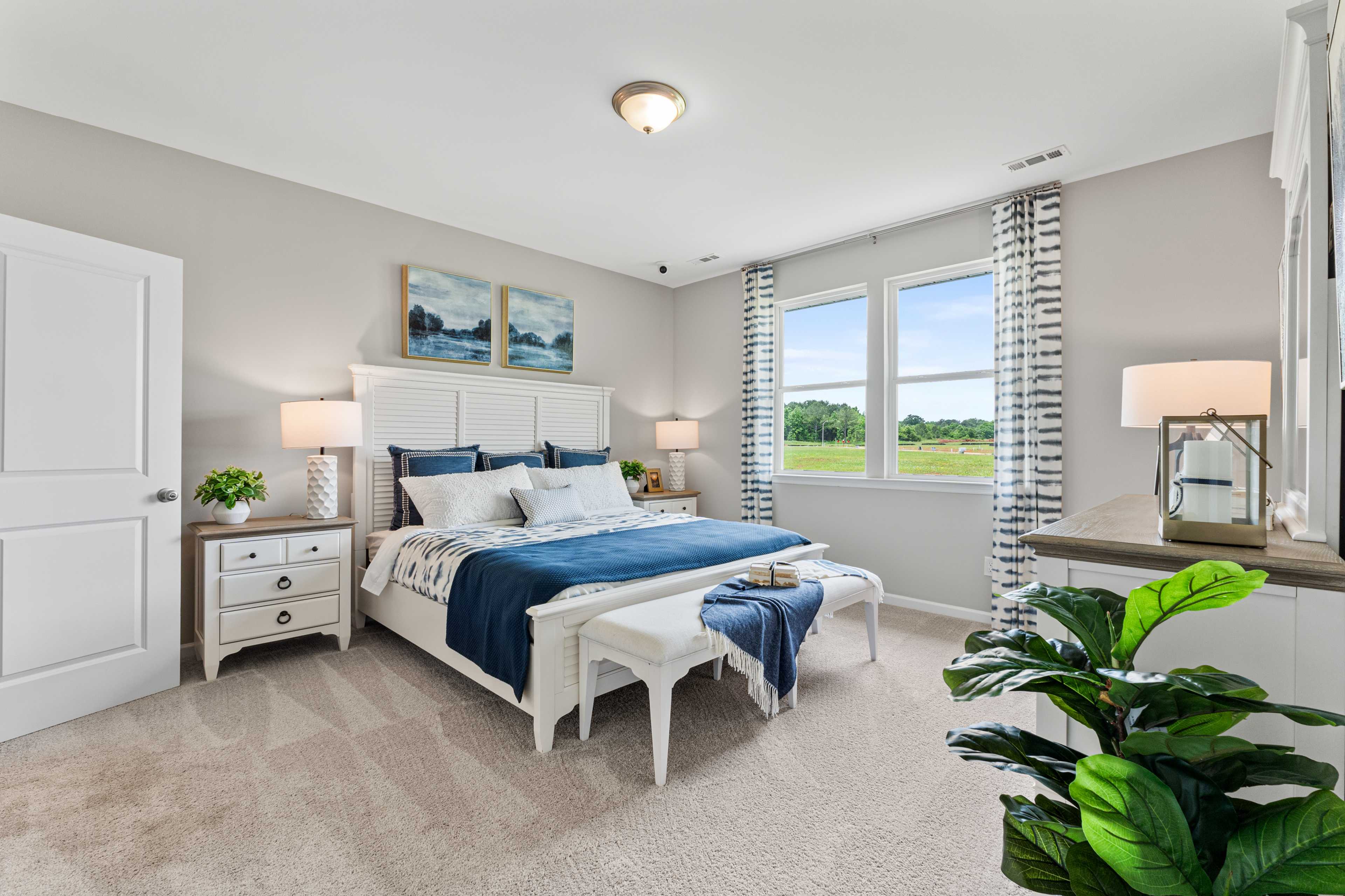 Spacious primary bedroom in Forest Glen, Hazel Green AL with king bed, blue bedding, large window overlooking fields, and modern white furniture