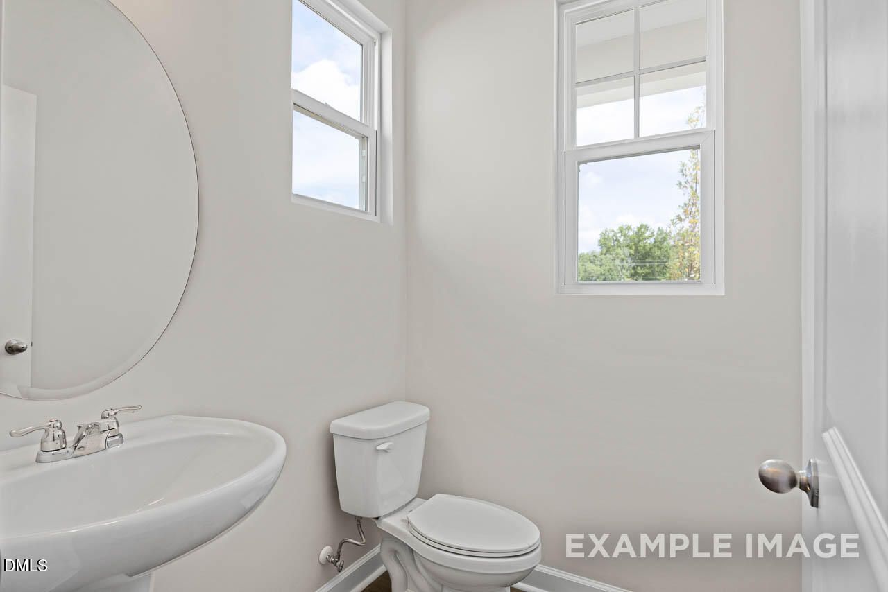 Bright powder room with pedestal sink, oval mirror, and window in The Graham home at Springvale, Fuquay-Varina, NC.