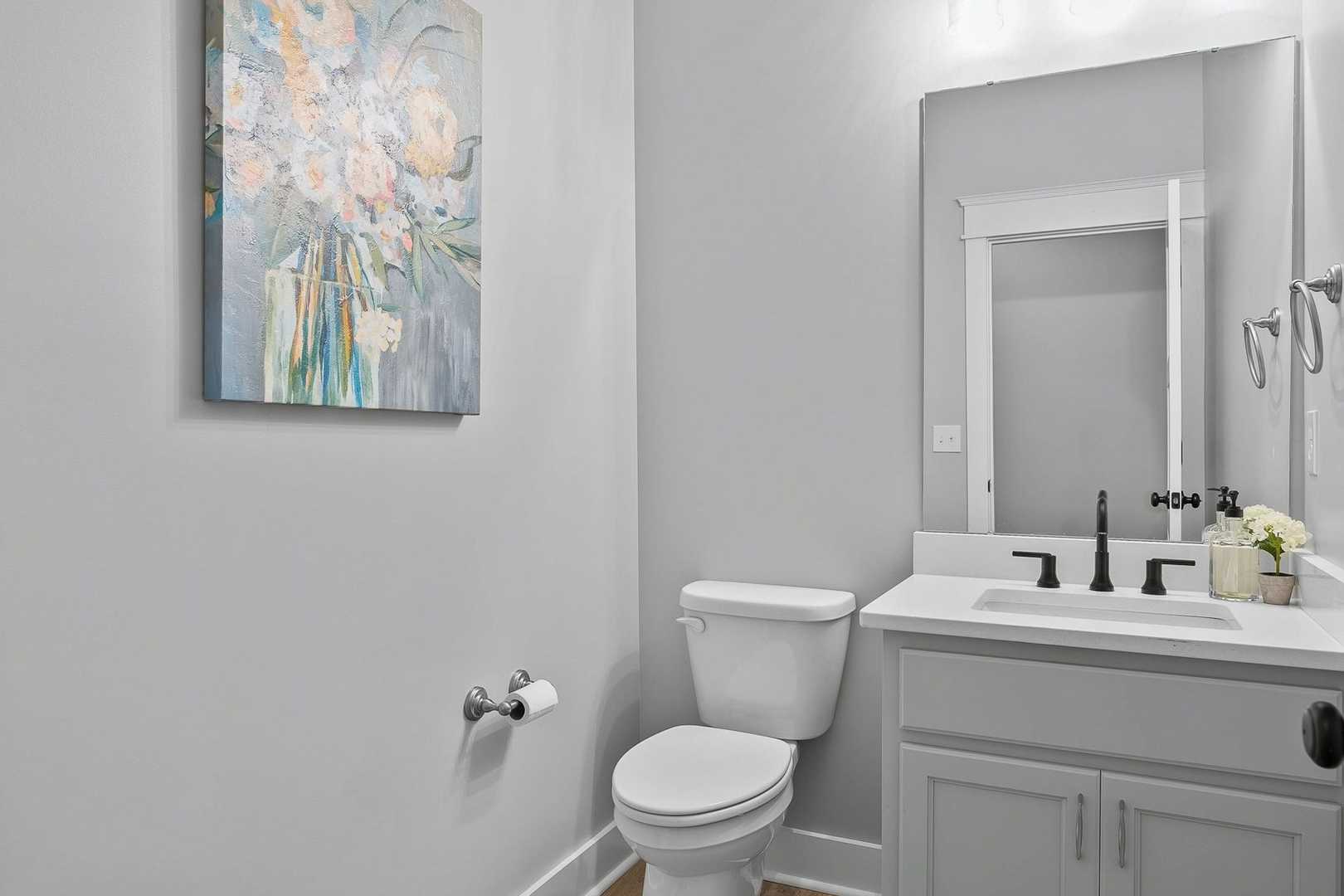 Serene powder room in The Oxford home design featuring gray walls, modern vanity sink, white toilet, and floral wall art