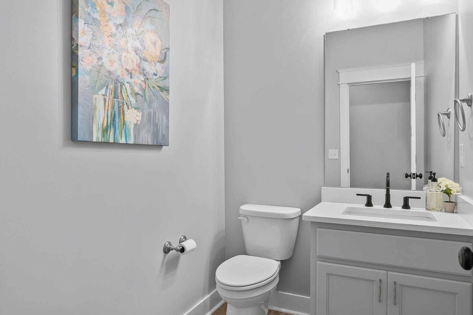 Serene powder room in The Oxford home design featuring gray walls, modern vanity sink, white toilet, and floral wall art