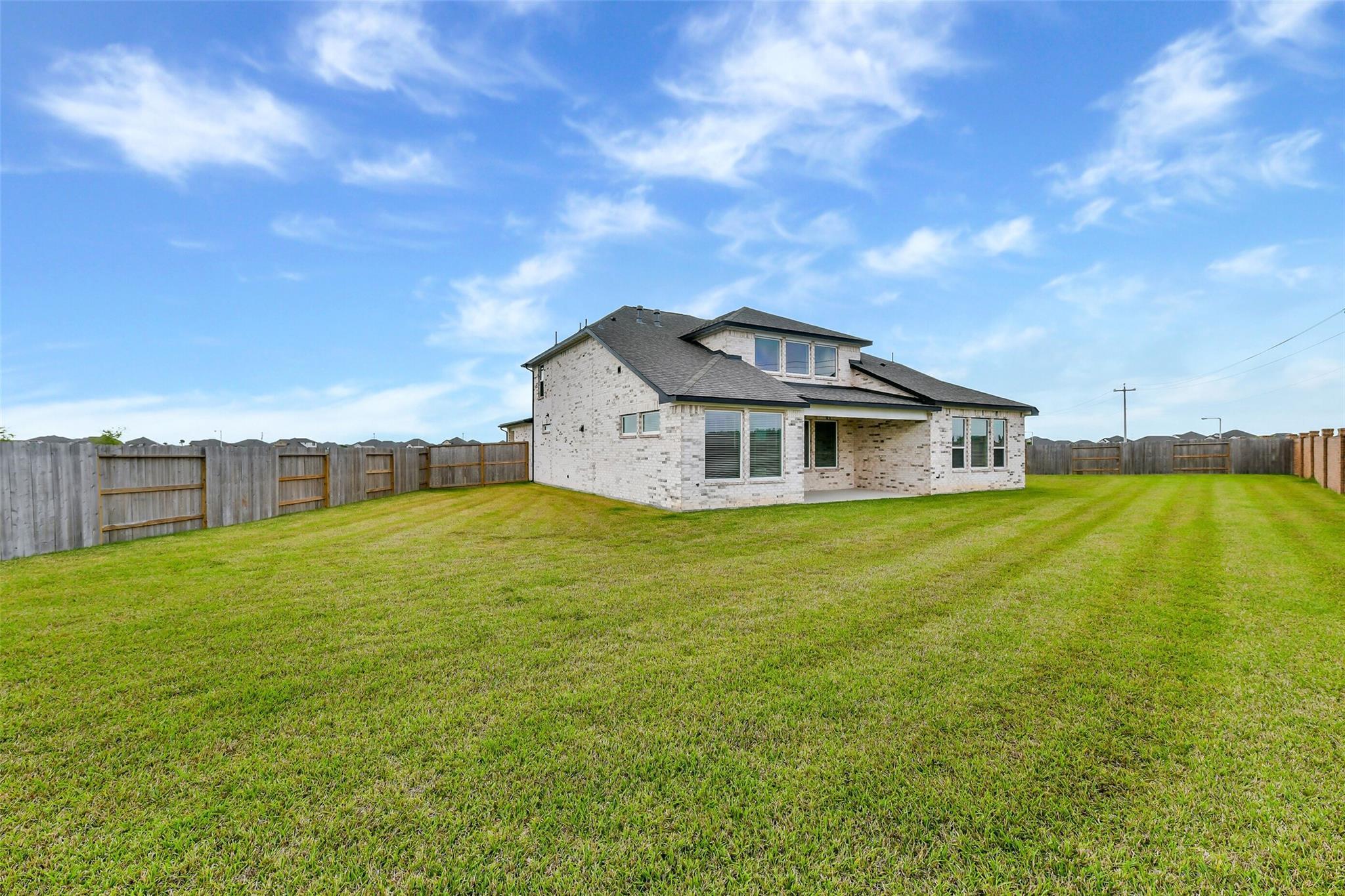 Two-story white brick home with covered patio, expansive green backyard, and wooden fence in Lago Mar, Texas City