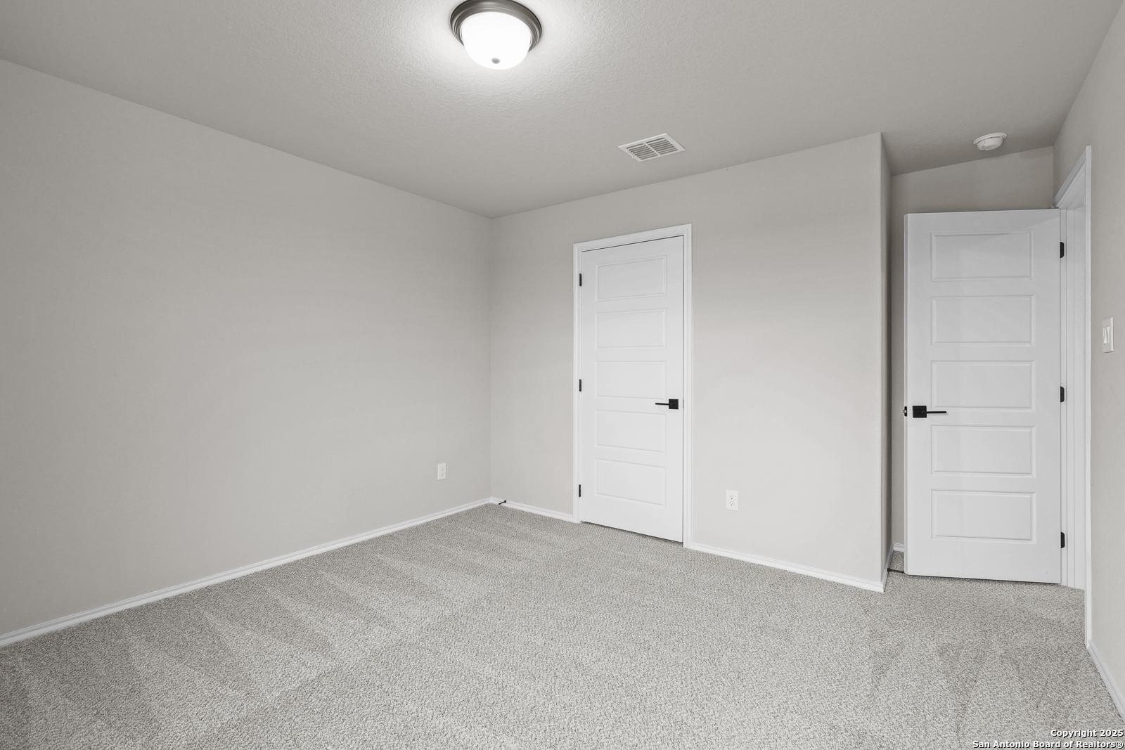 Empty secondary bedroom featuring gray walls, carpeted floor, and two white doors in Davidson Homes The Murray J, San Antonio, Texas