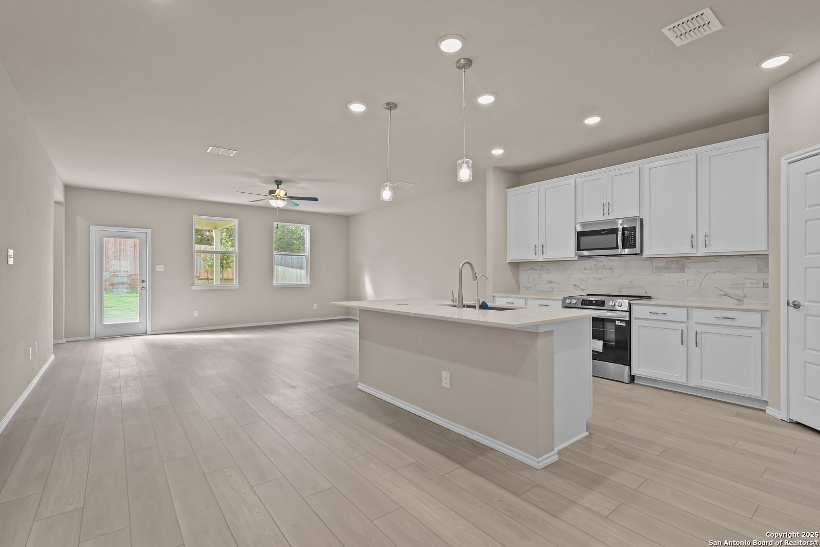 Modern open-concept kitchen with white cabinets, island sink, stainless appliances, and light wood floors in Davidson Homes The Douglas G, San Antonio
