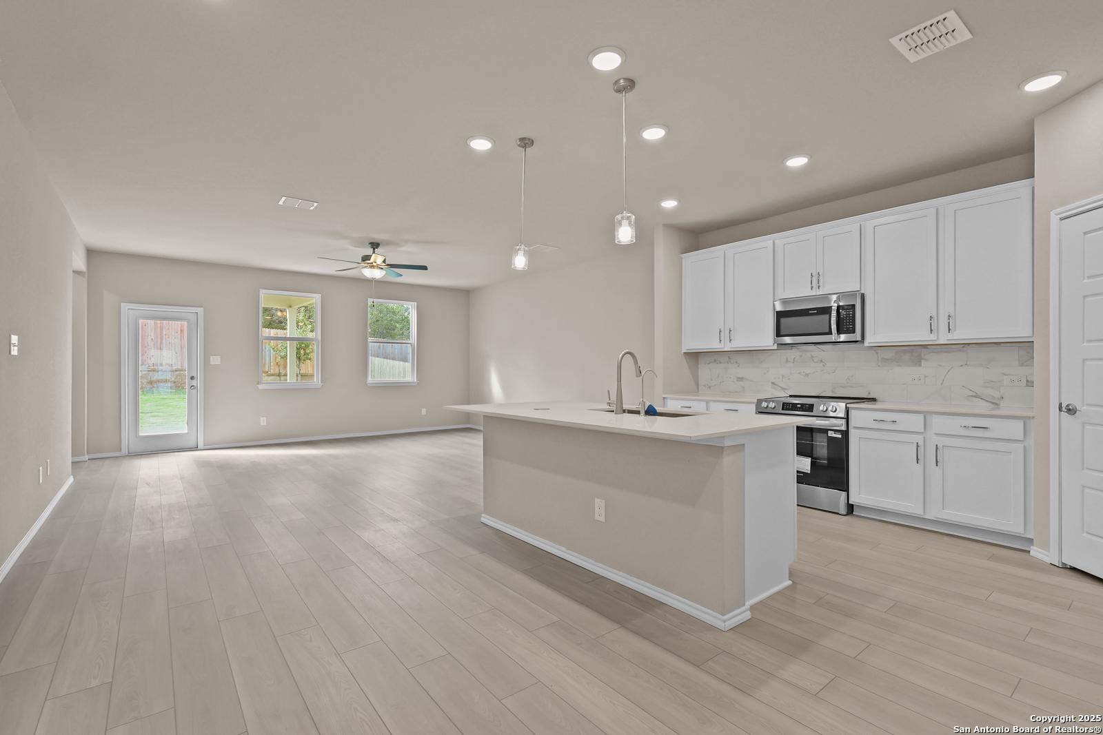 Modern open-concept kitchen with white cabinets, island sink, stainless appliances, and light wood floors in Davidson Homes The Douglas G, San Antonio
