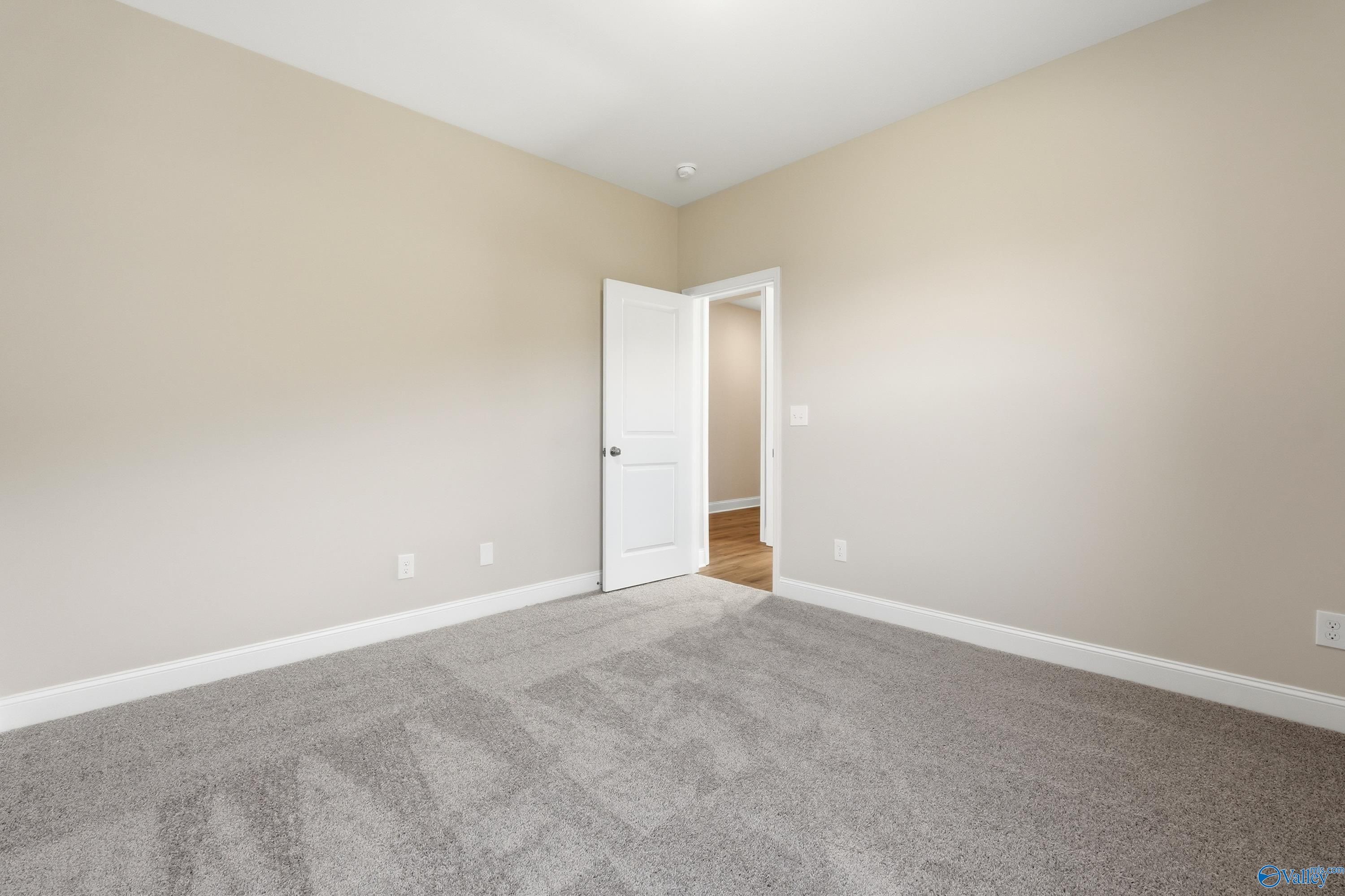 Spacious secondary bedroom featuring beige walls, gray carpet, and open door in Davidson Homes The Everett, Creekside, Harvest, Alabama
