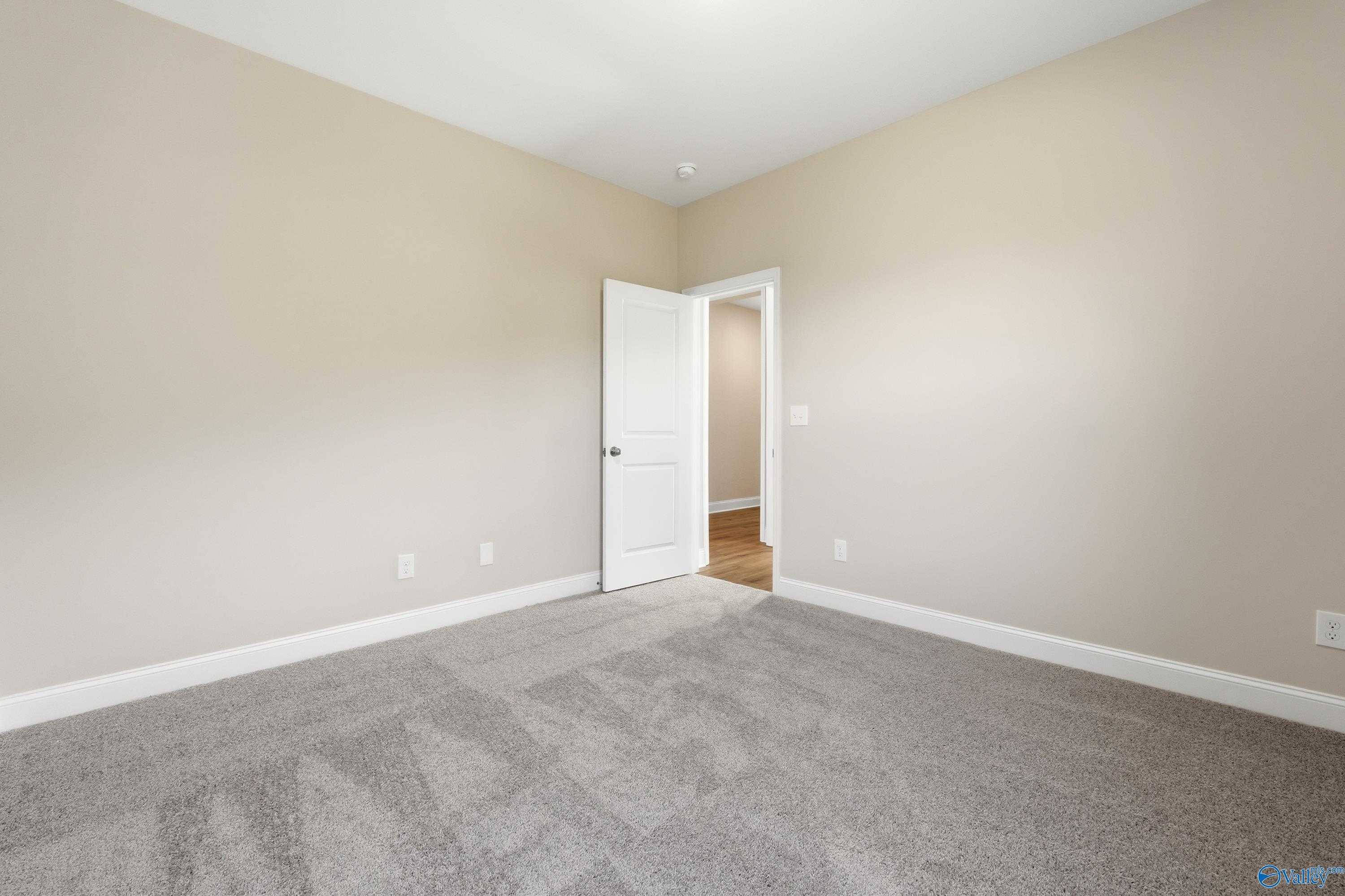 Spacious secondary bedroom featuring beige walls, gray carpet, and open door in Davidson Homes The Everett, Creekside, Harvest, Alabama