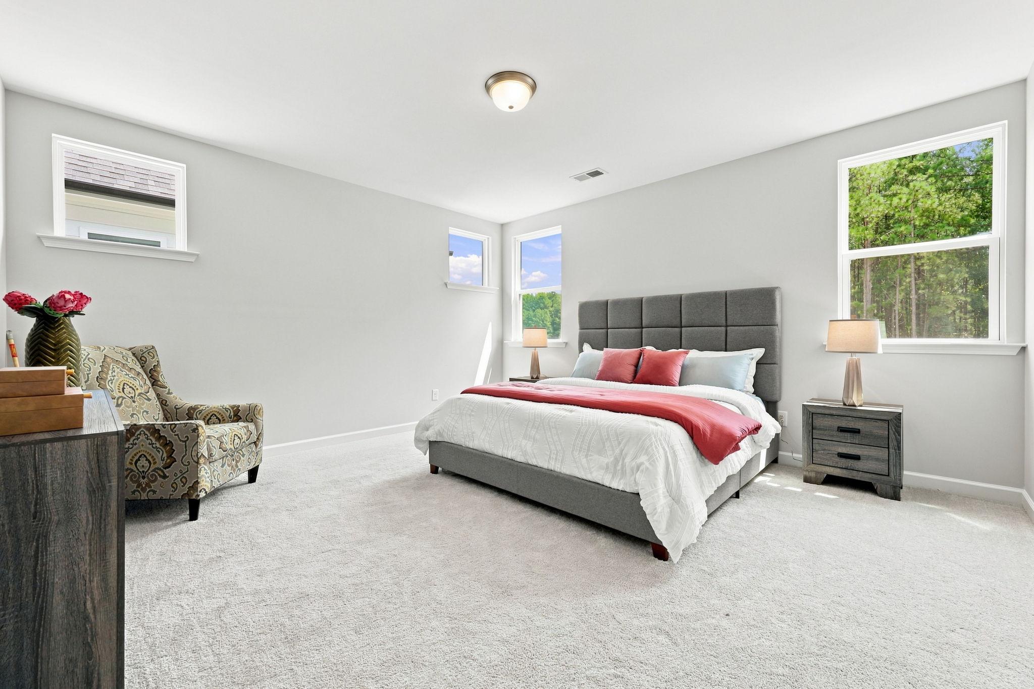 Spacious master bedroom in The Jordan A featuring a plush upholstered bed, cozy sitting area, and ample natural light.