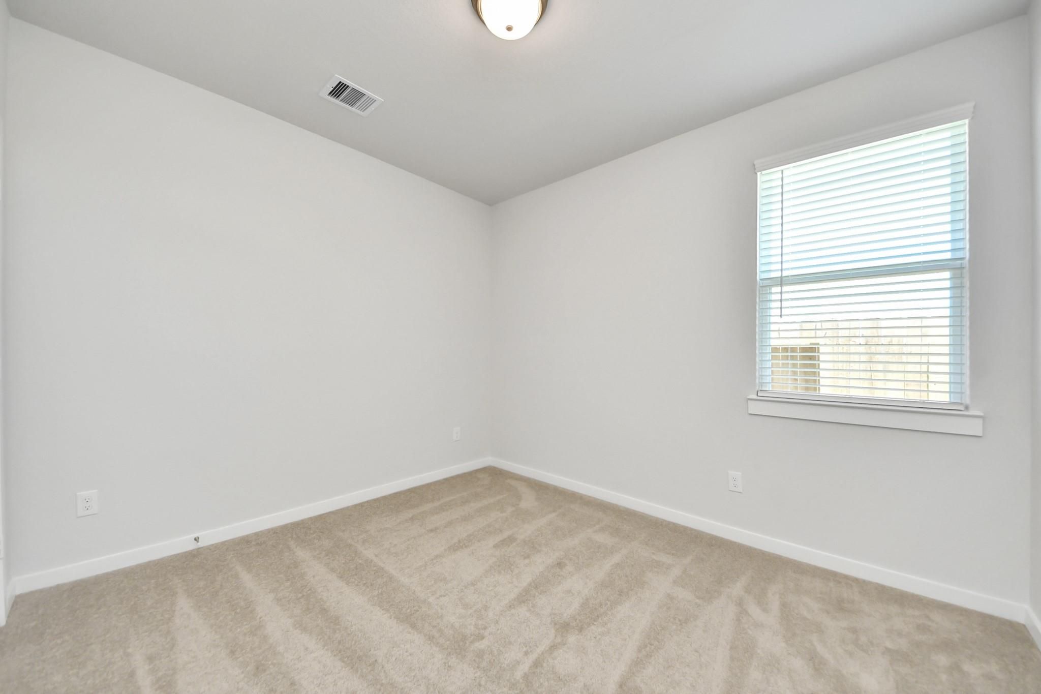 Bright bedroom with beige carpet, white walls, and window with blinds in Davidson Homes The Costa A plan, Emberly, Beasley, TX