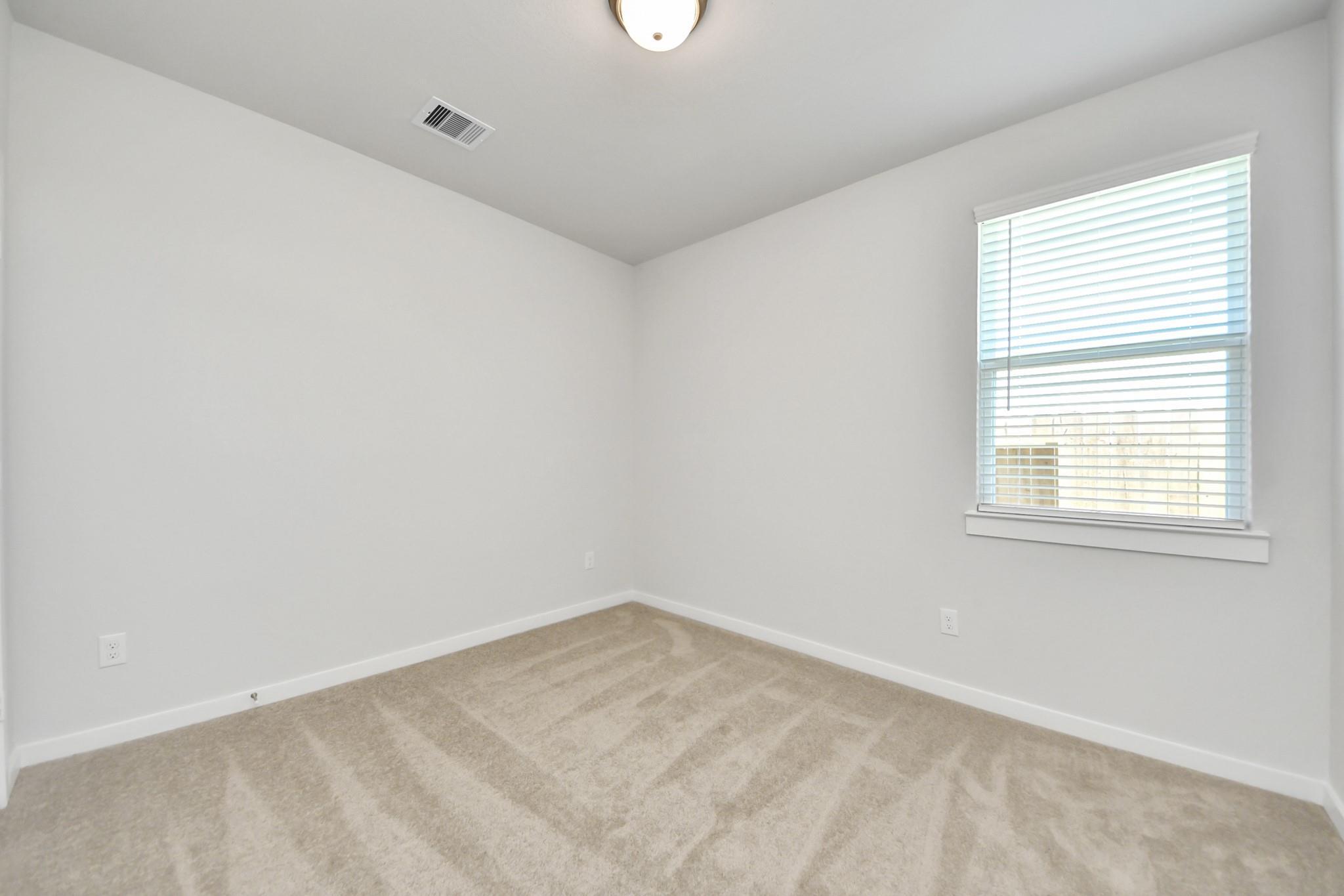 Bright bedroom with beige carpet, white walls, and window with blinds in Davidson Homes The Costa A plan, Emberly, Beasley, TX