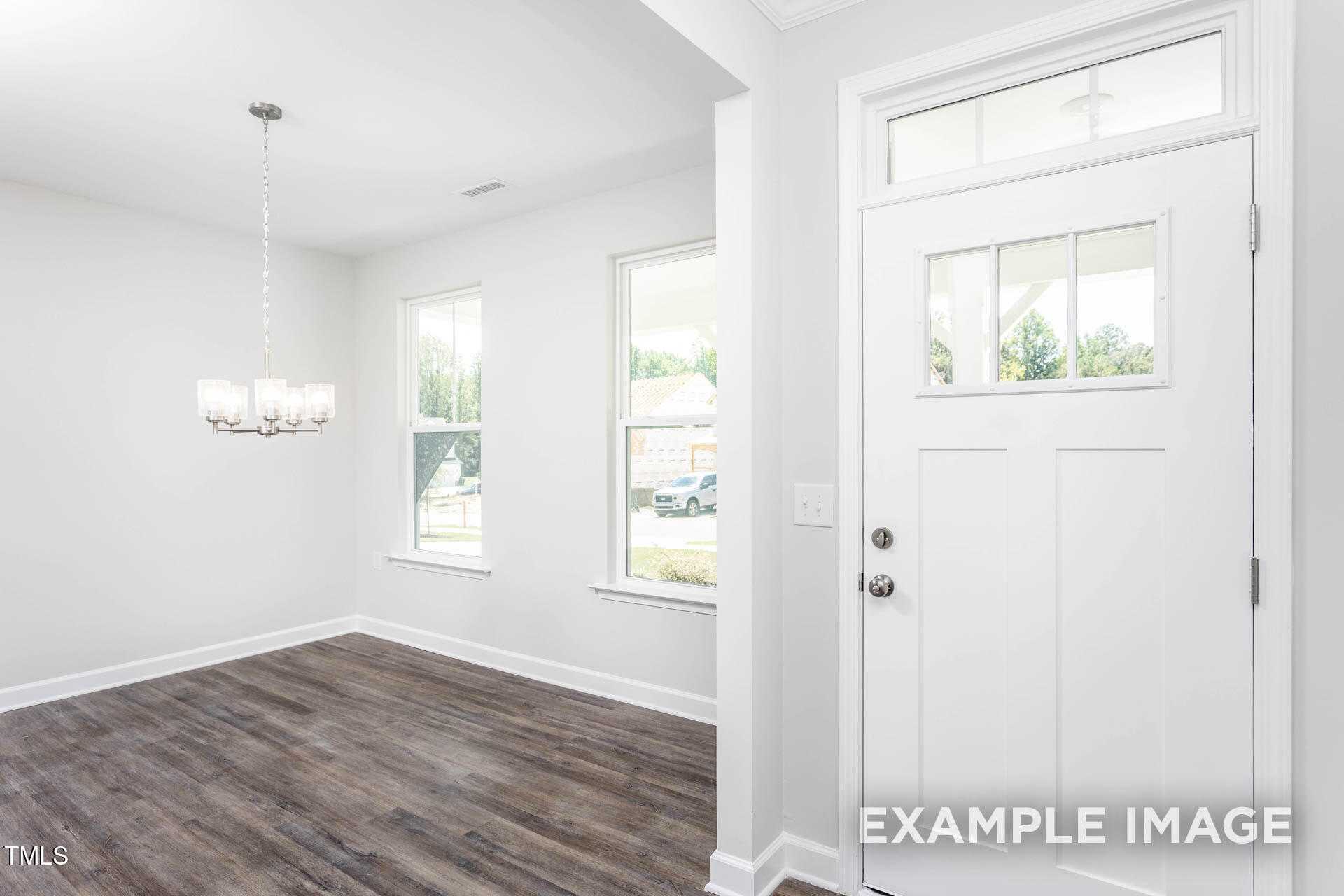 Bright entry foyer with chandelier, hardwood floors, large windows, and white front door in Davidson Homes The Willow B, Lillington, NC
