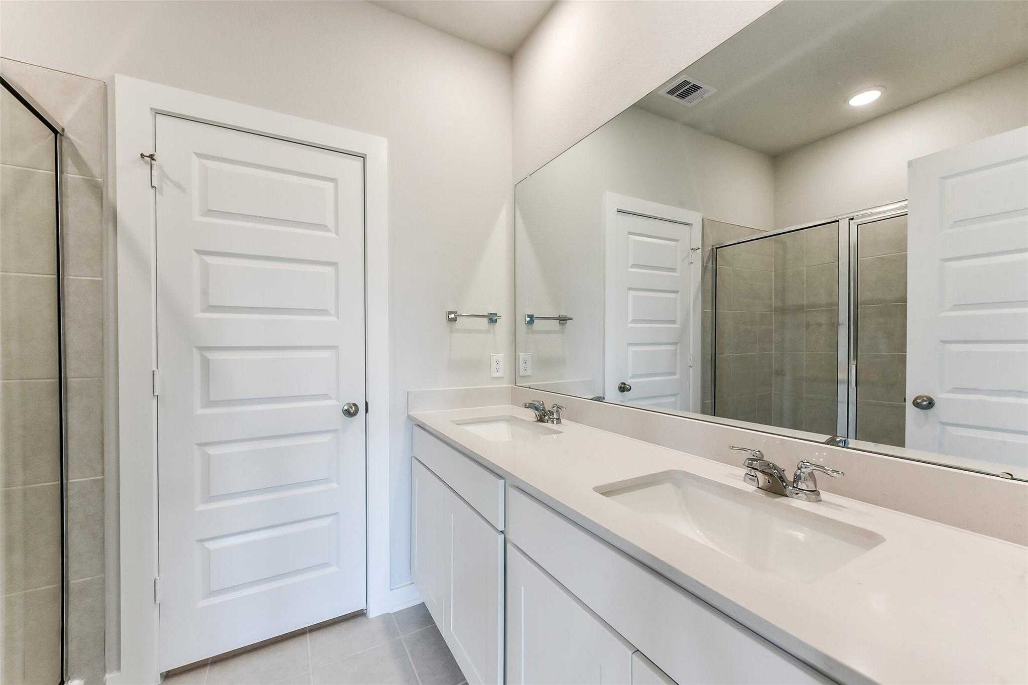 Modern double vanity with dual sinks, mirrors, and glass shower in Davidson Homes The Frio F master bath, Dayton, Texas