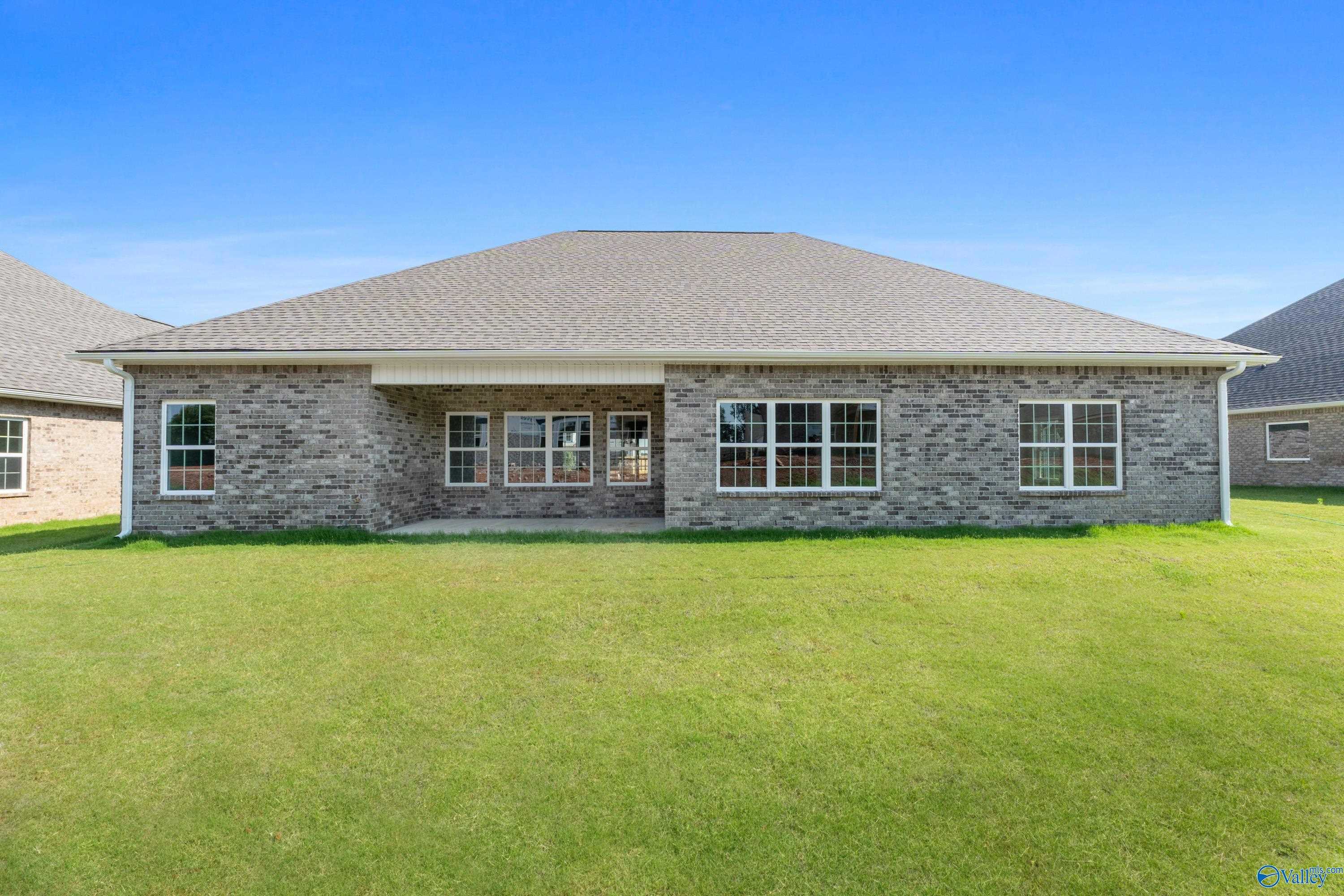 Single-story brick home rear with covered patio, large windows, and lush green lawn in Kendall Farms, Toney, Alabama