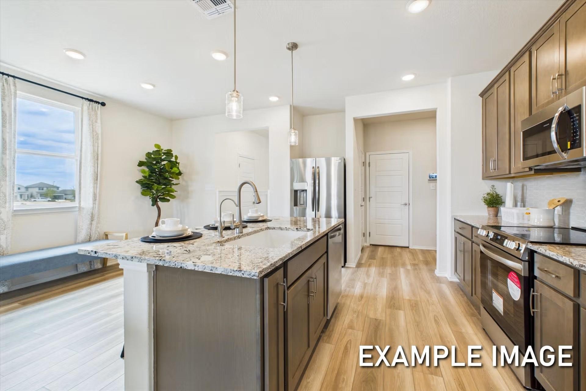 Modern kitchen with granite island and stainless steel appliances in The Brazos E floor plan at Heartland, Texas.