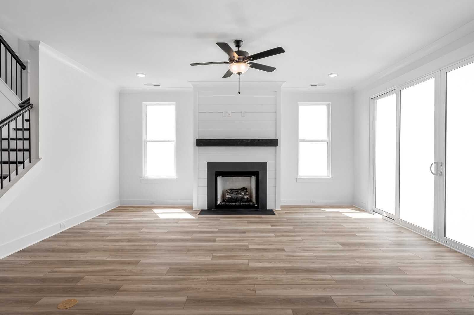 Bright living room with shiplap fireplace, hardwood floors, ceiling fan, and sliding doors in Davidson Homes The Hathaway, Murfreesboro