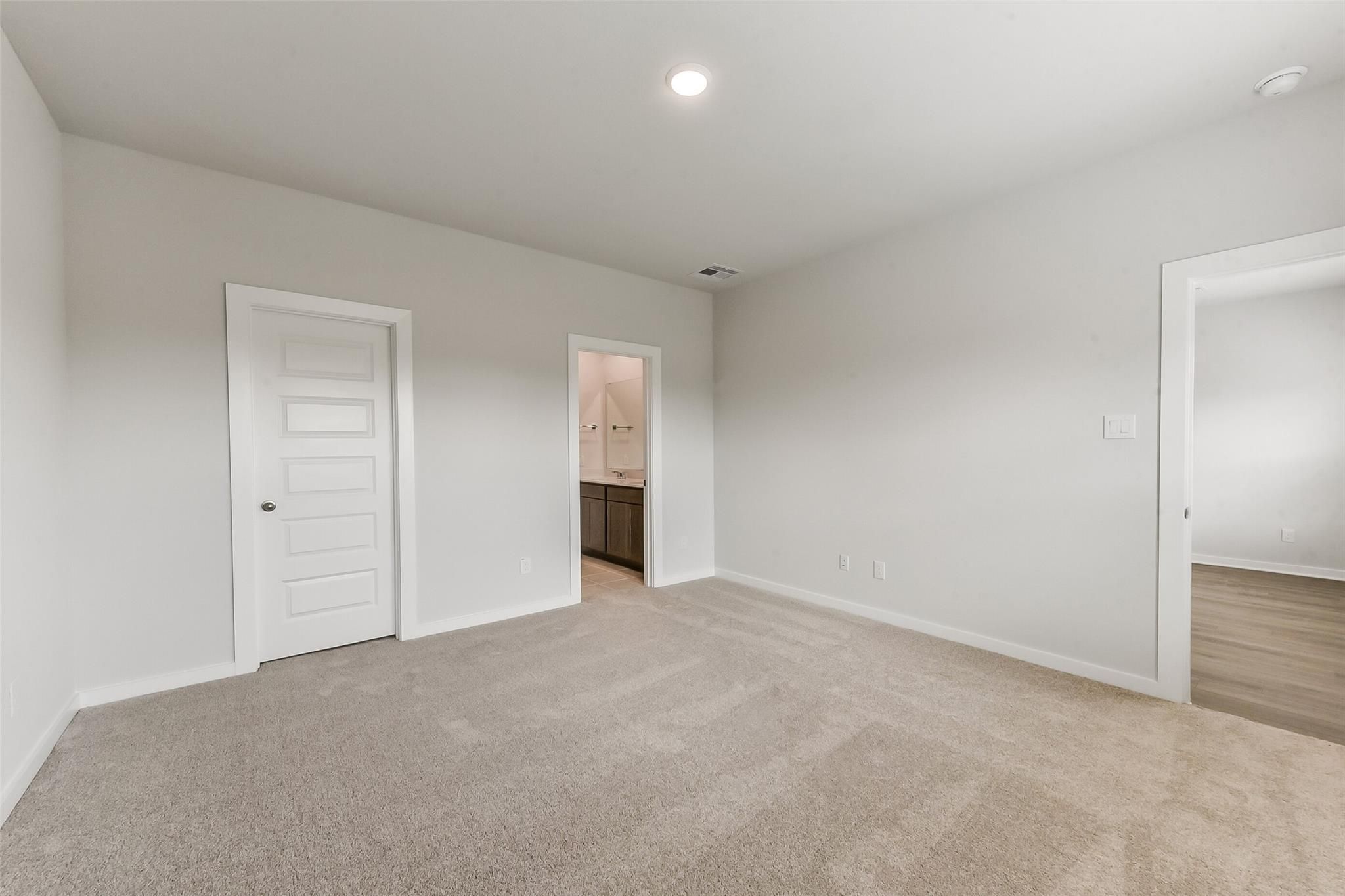 Spacious bedroom with en-suite bathroom, beige carpet, and light gray walls in Davidson Homes The Sabine F, Dayton Texas