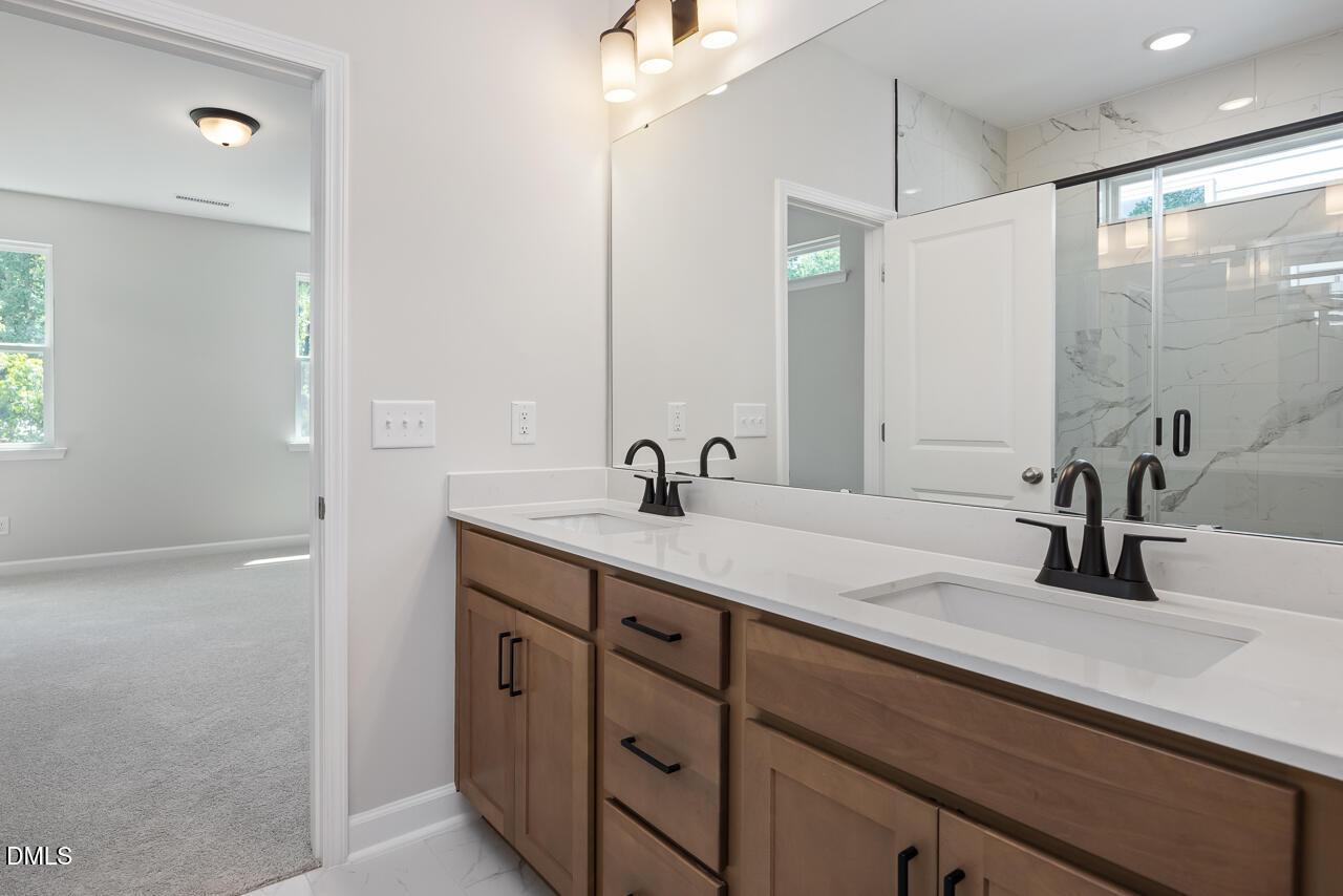 Modern primary bathroom with double vanity, quartz countertops, and walk-in shower in The Ashport L at Sage on North Main.