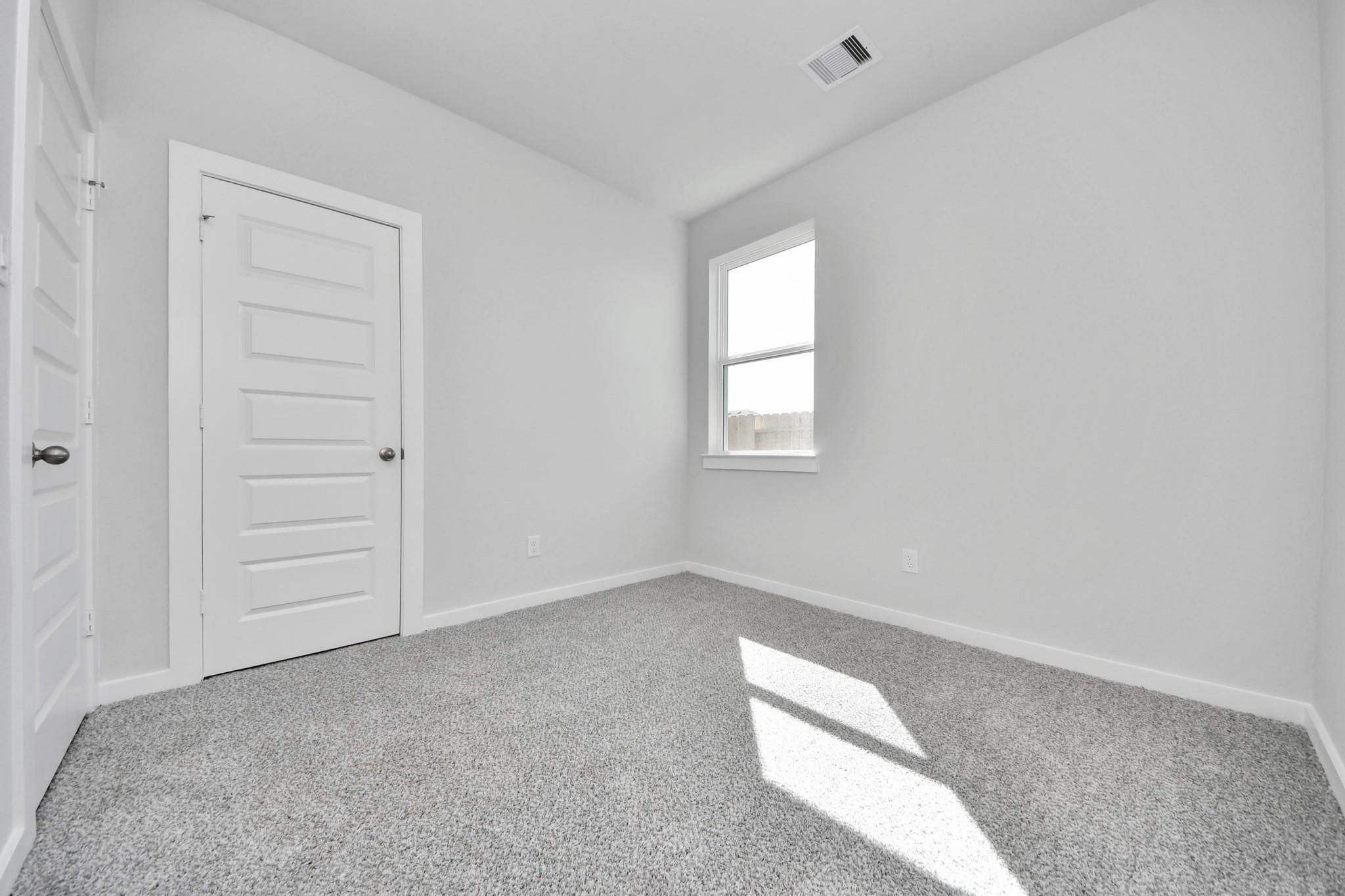 Bright bedroom with neutral grey carpet and white walls in The Colorado G floor plan at Emberly in Beasley, Texas.