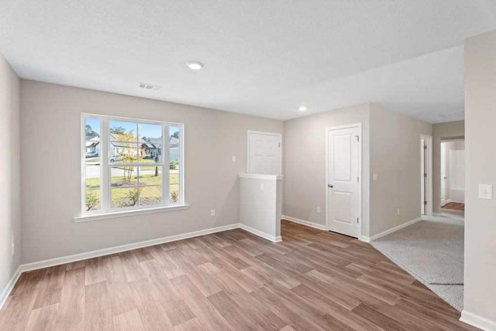Bright living room with large window view of neighborhood, hardwood floors, and neutral walls in Davidson Homes The Washington, Phenix City, AL