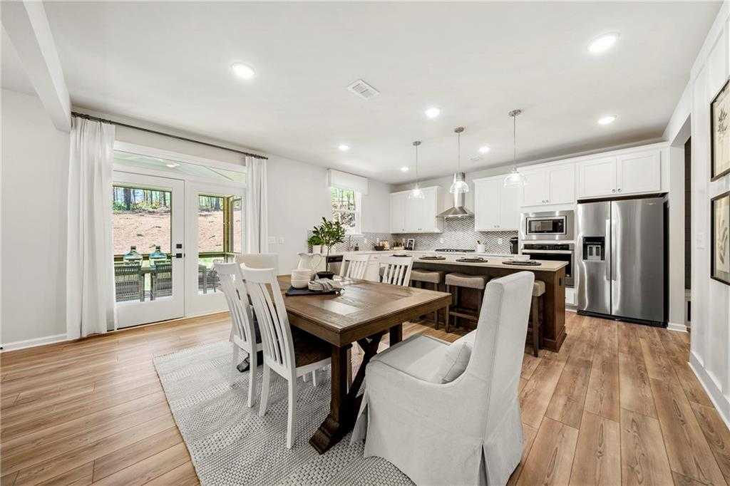 Open-concept dining and kitchen with wooden table, white cabinets, stainless appliances, French doors to patio in Davidson Homes The Hickory B, Riverwood, Dallas, Georgia