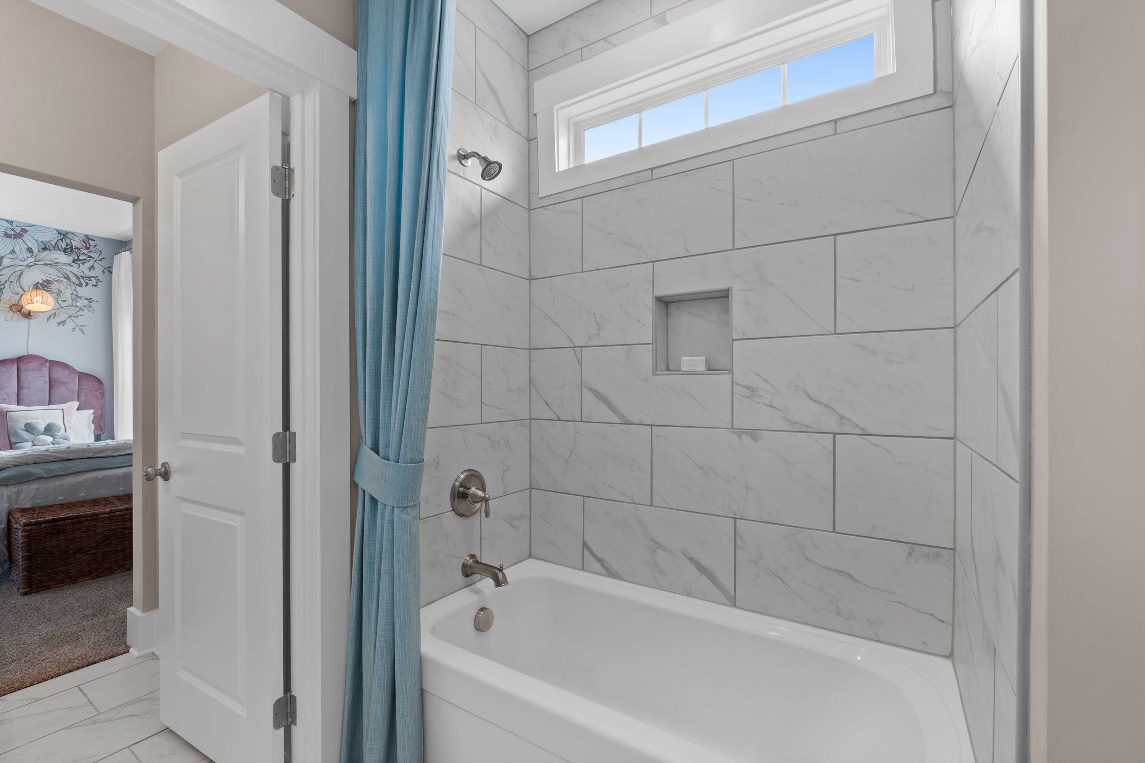Spacious bathroom with white subway tile walls, corner bathtub, blue shower curtain, and bedroom view at Creekside in Harvest, Alabama