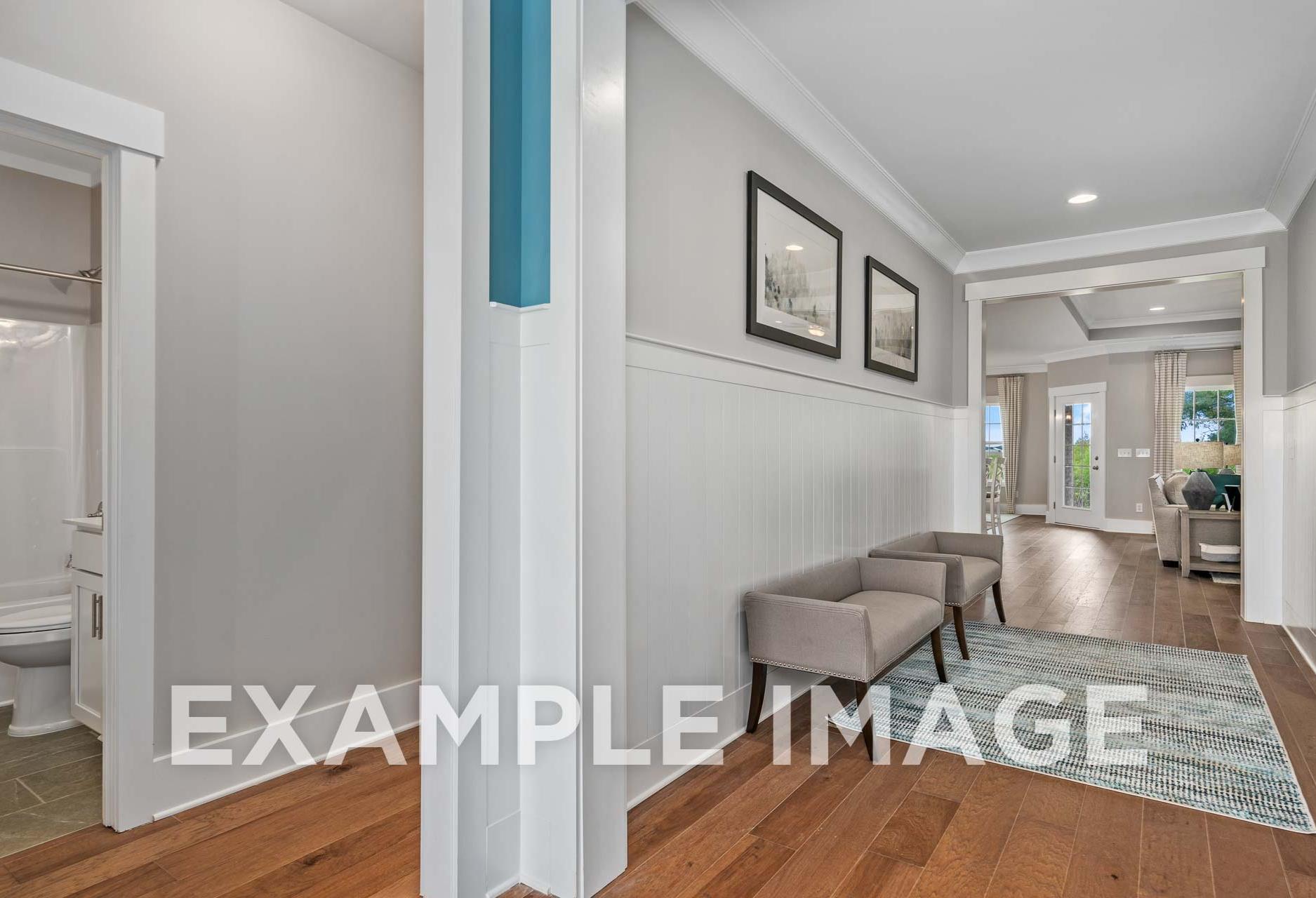 Spacious hallway in The Harrison home design with wood floors, wainscoting, adjacent bathroom, and modern seating