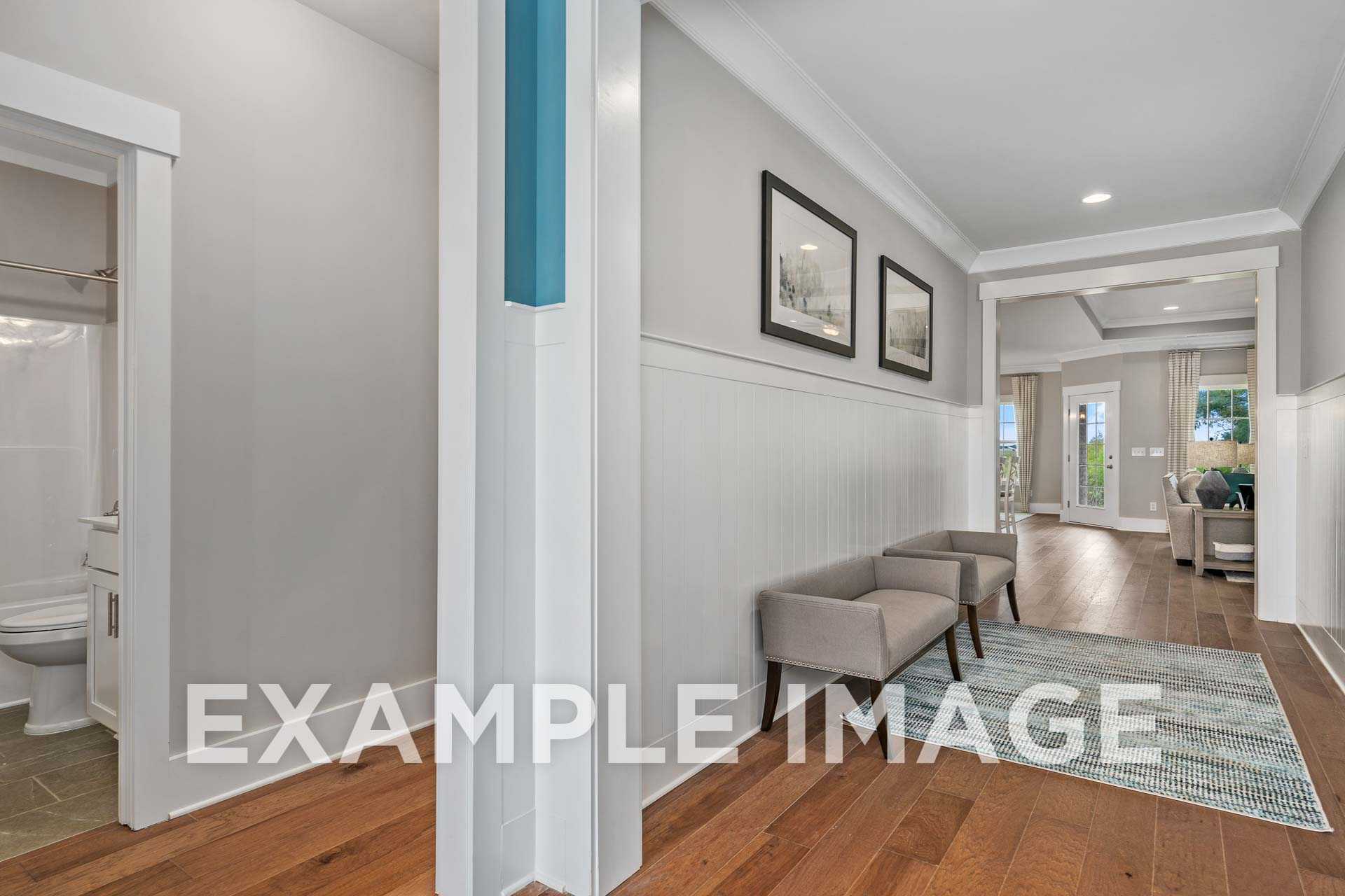 Spacious hallway in The Harrison home design with adjacent bathroom, gray walls, hardwood floors, and accent seating