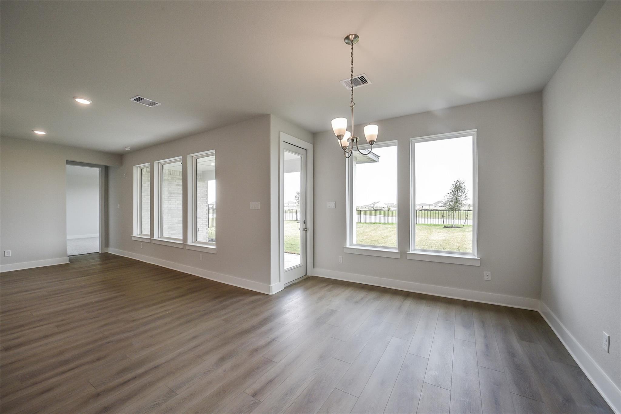 Bright family room with chandelier, hardwood floors, and large windows overlooking grassy yard in Davidson Homes The Philip B, Rosharon, Texas