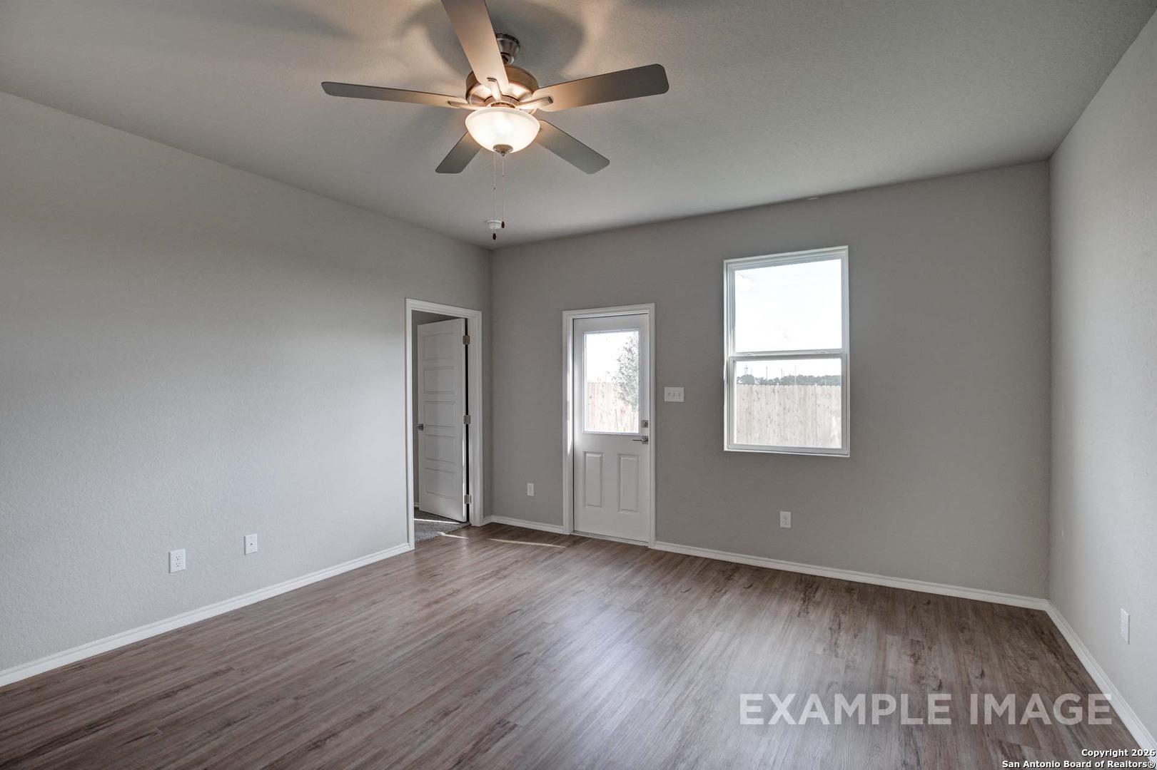 Bright living room with hardwood floors, ceiling fan, large windows, and back door in Davidson Homes The Frio C, San Antonio