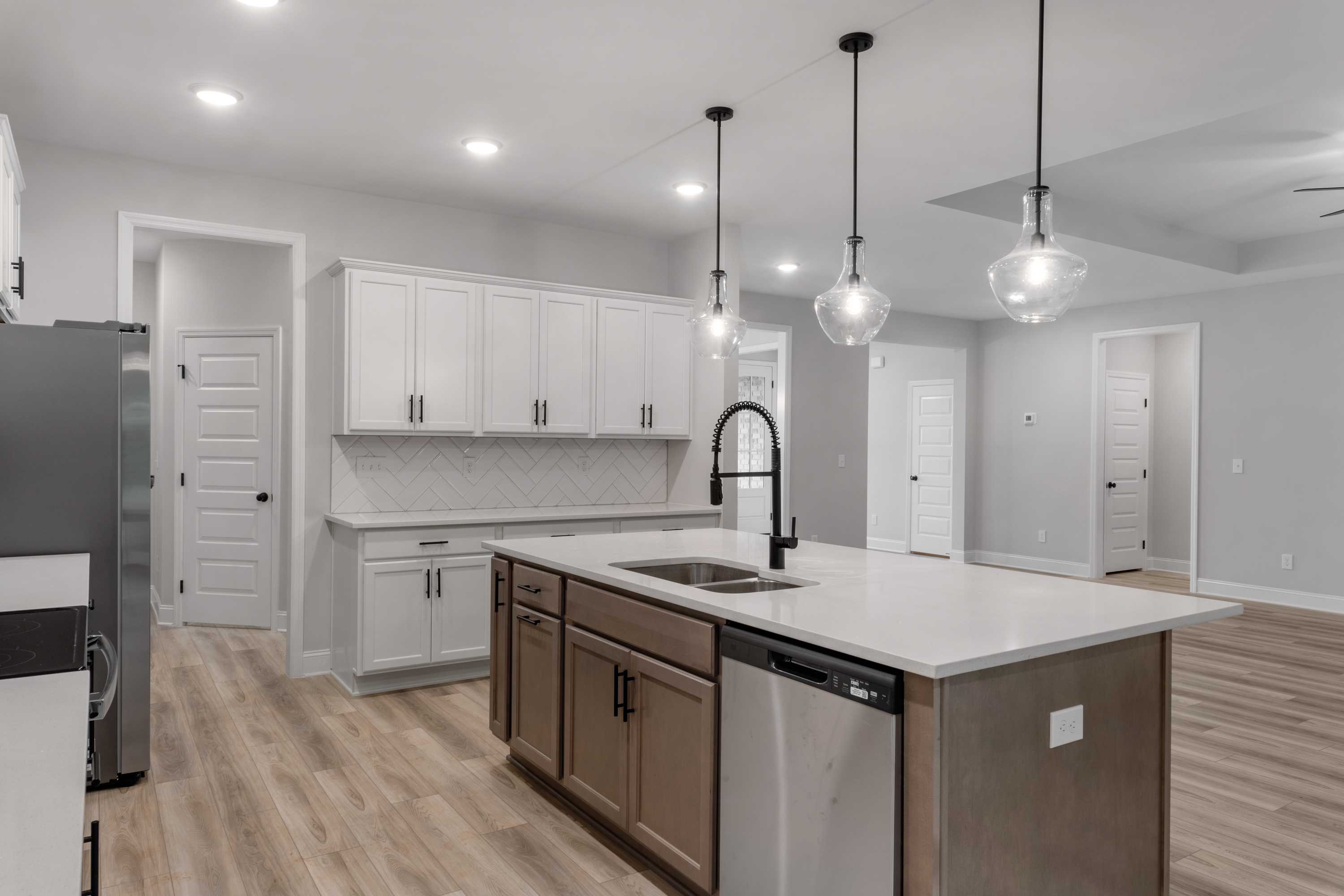 Spacious kitchen in The Oxford Davidson Homes plan featuring white shaker cabinets, large quartz island with farmhouse sink, and pendant lights