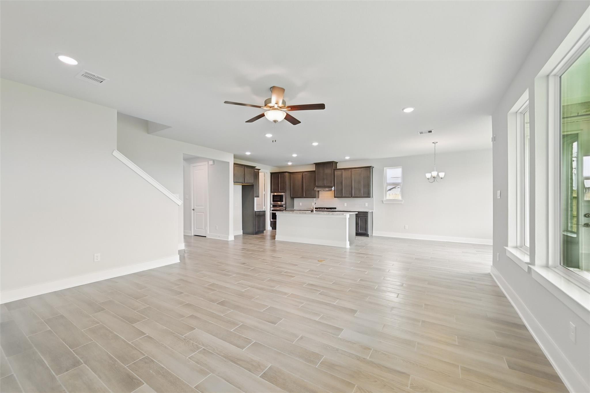 Open-concept kitchen with large island, wood cabinets, and staircase in Davidson Homes The Philip A, Lago Mar, Texas City