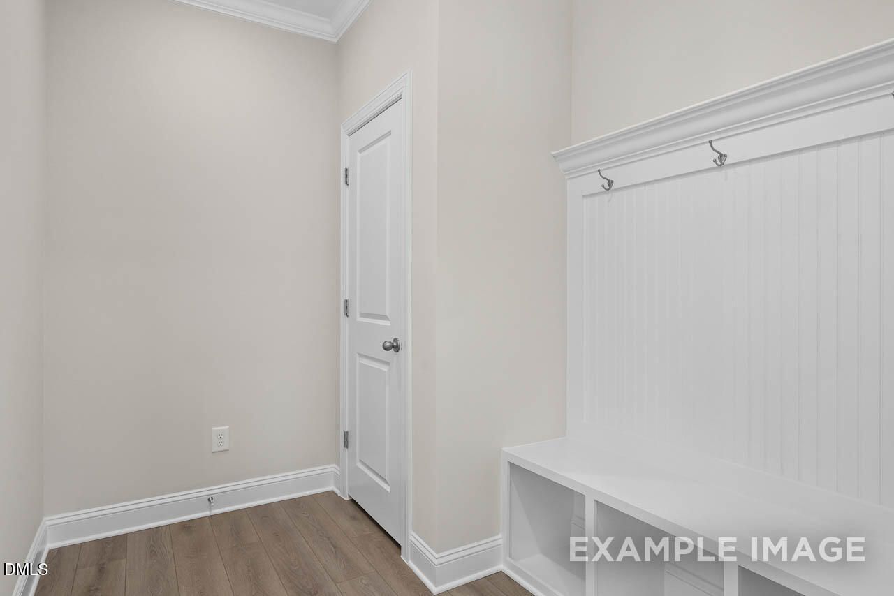 Spacious mudroom with white paneled bench, coat hooks, hardwood floors in Davidson Homes The Aspen C, Apex, NC