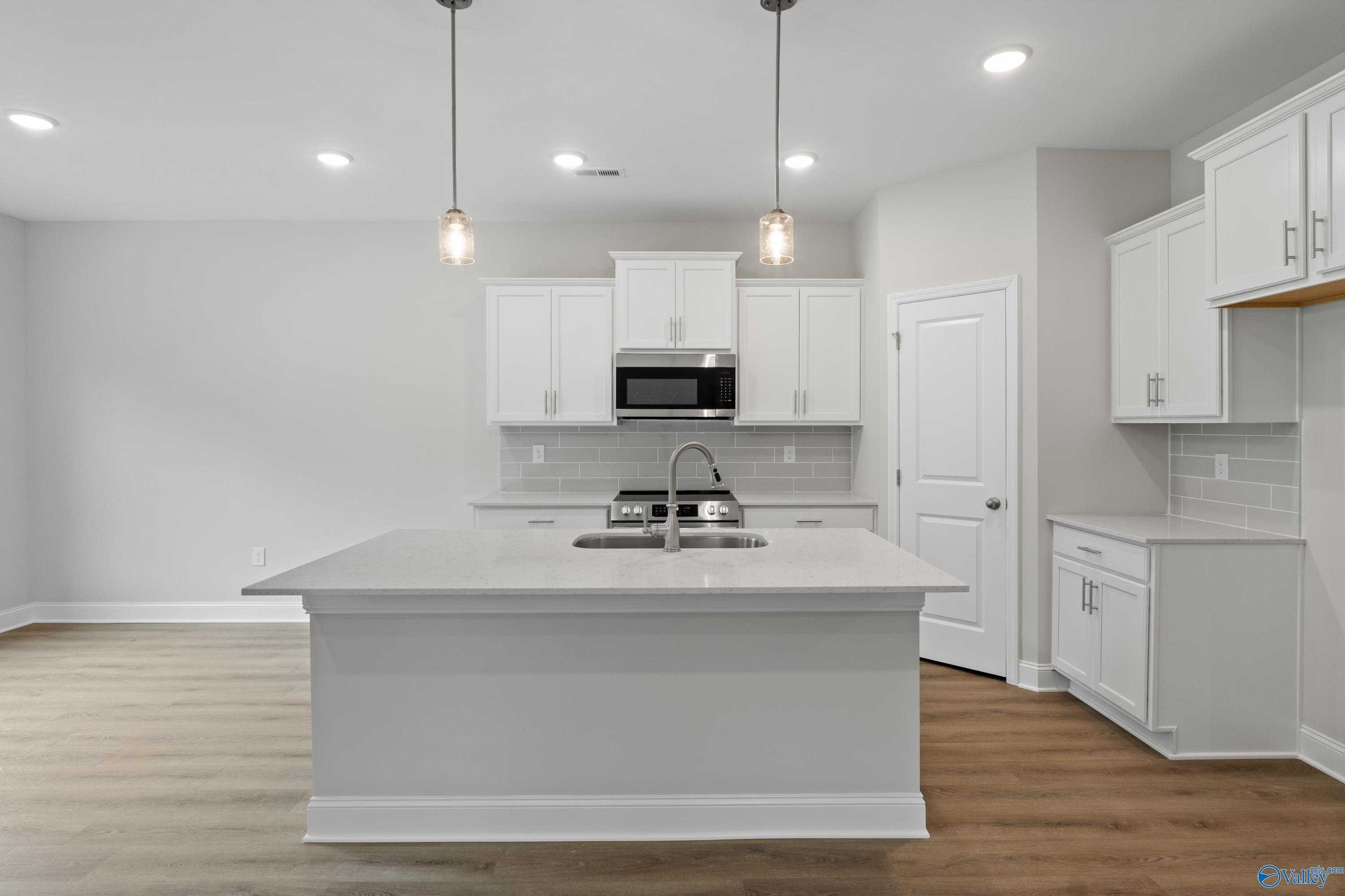 Modern white kitchen island with sink, stainless microwave, subway tile backsplash in The Asheville C, Davidson Homes Huntsville AL