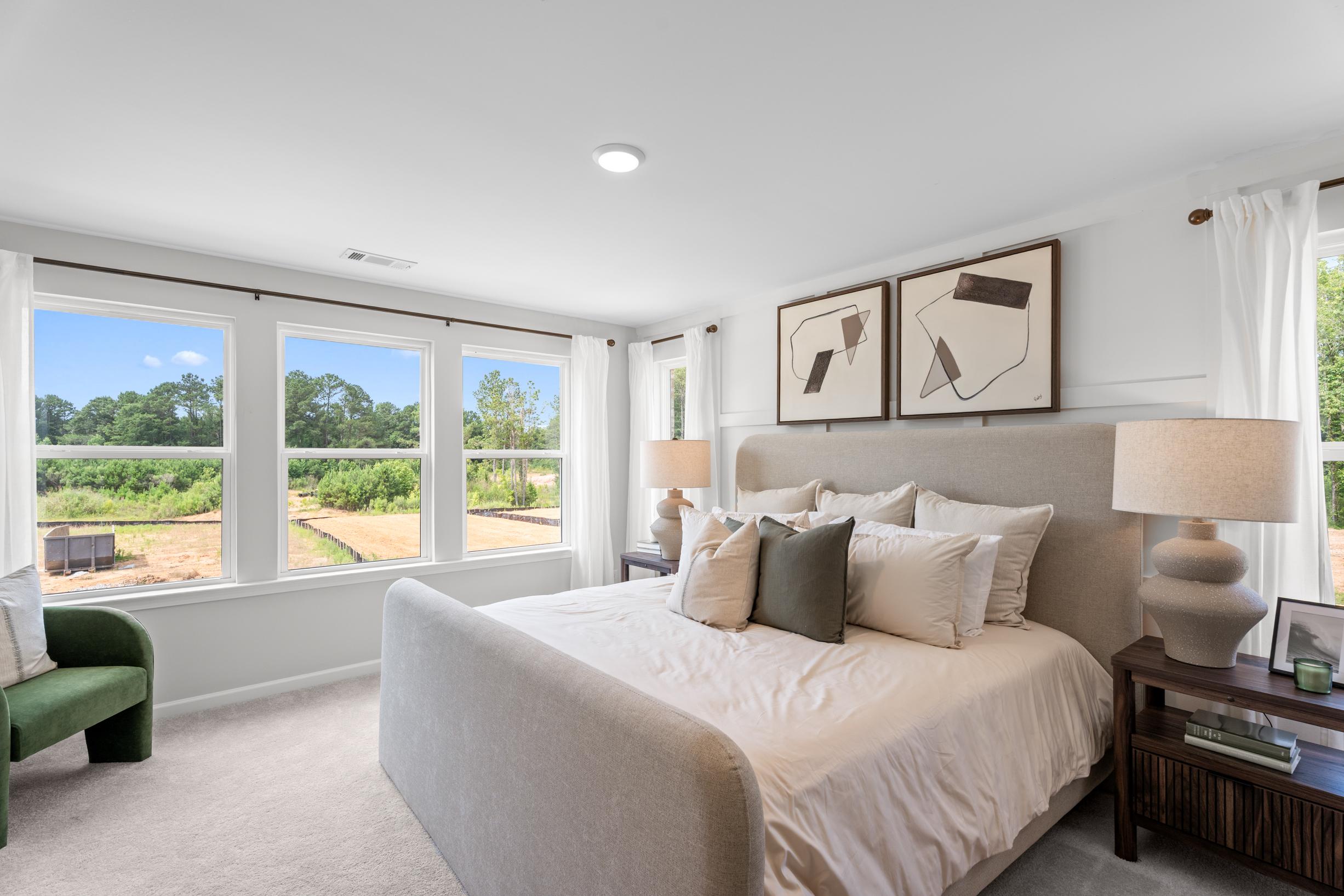 Spacious primary bedroom at Links Crossing in Auburn, AL, featuring a plush upholstered bed and views of the community.