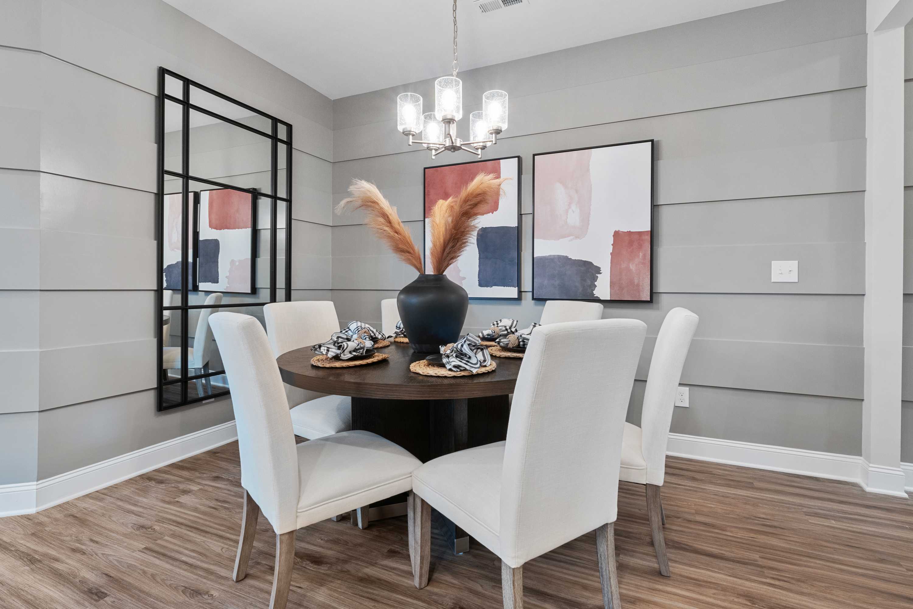 Contemporary dining room at The Retreat at Cain Park in Hartselle Alabama featuring round wood table white chairs abstract art pampas grass centerpiece shiplap walls and hardwood floors