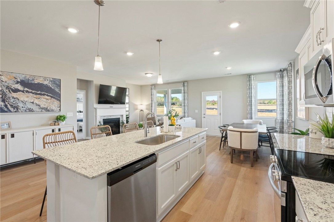 Open-concept kitchen with white shaker cabinets, quartz island sink, stainless appliances, dining nook, and living area in Davidson Homes Phoenix B, Opelika