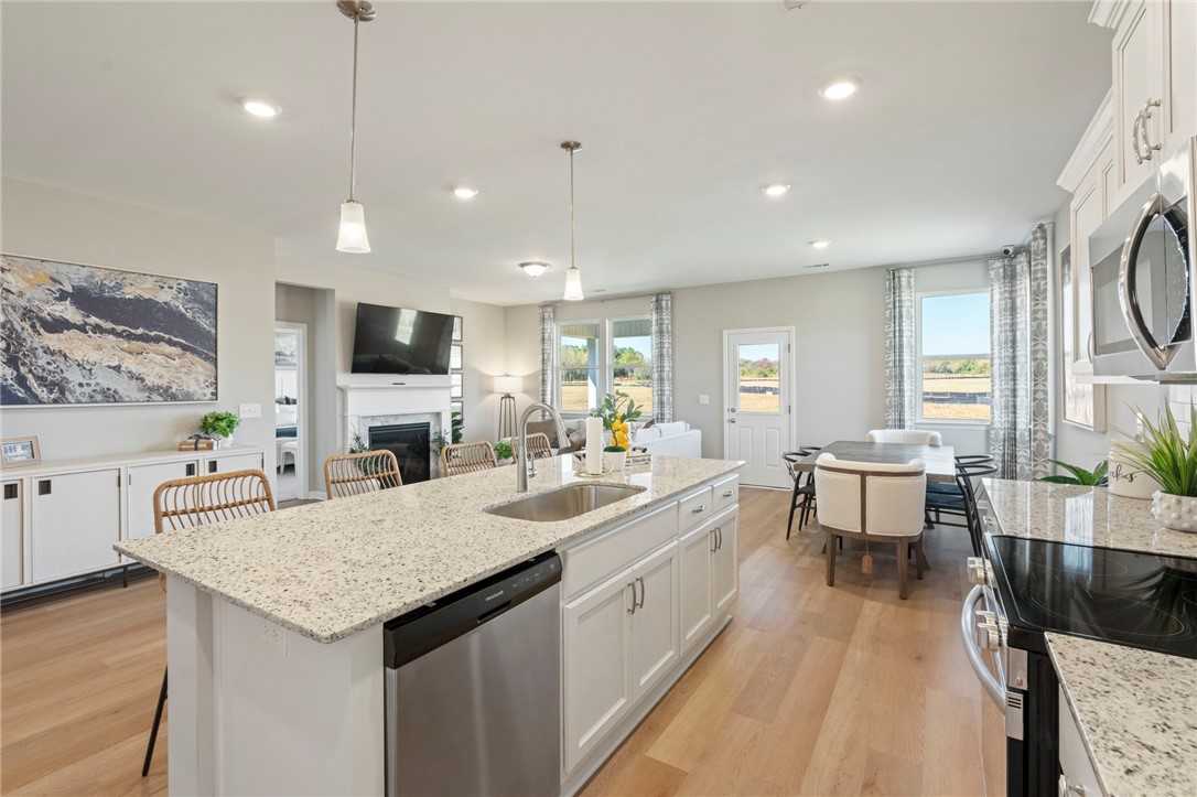 Open-concept kitchen with white shaker cabinets, quartz island sink, stainless appliances, dining nook, and living area in Davidson Homes Phoenix B, Opelika
