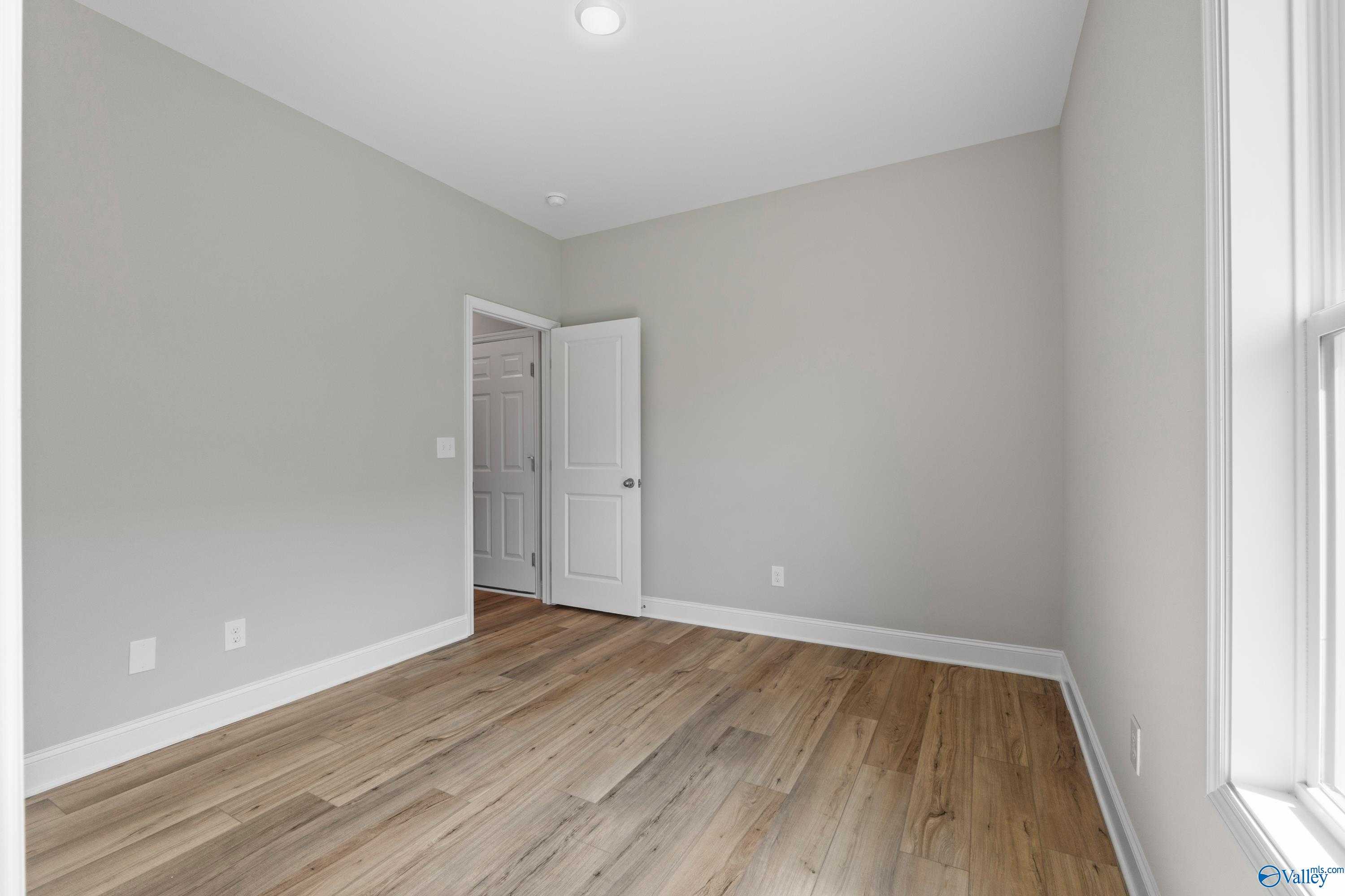 Spacious empty bedroom with light gray walls, hardwood floors, and window in Davidson Homes The Daphne C, Athens, Alabama