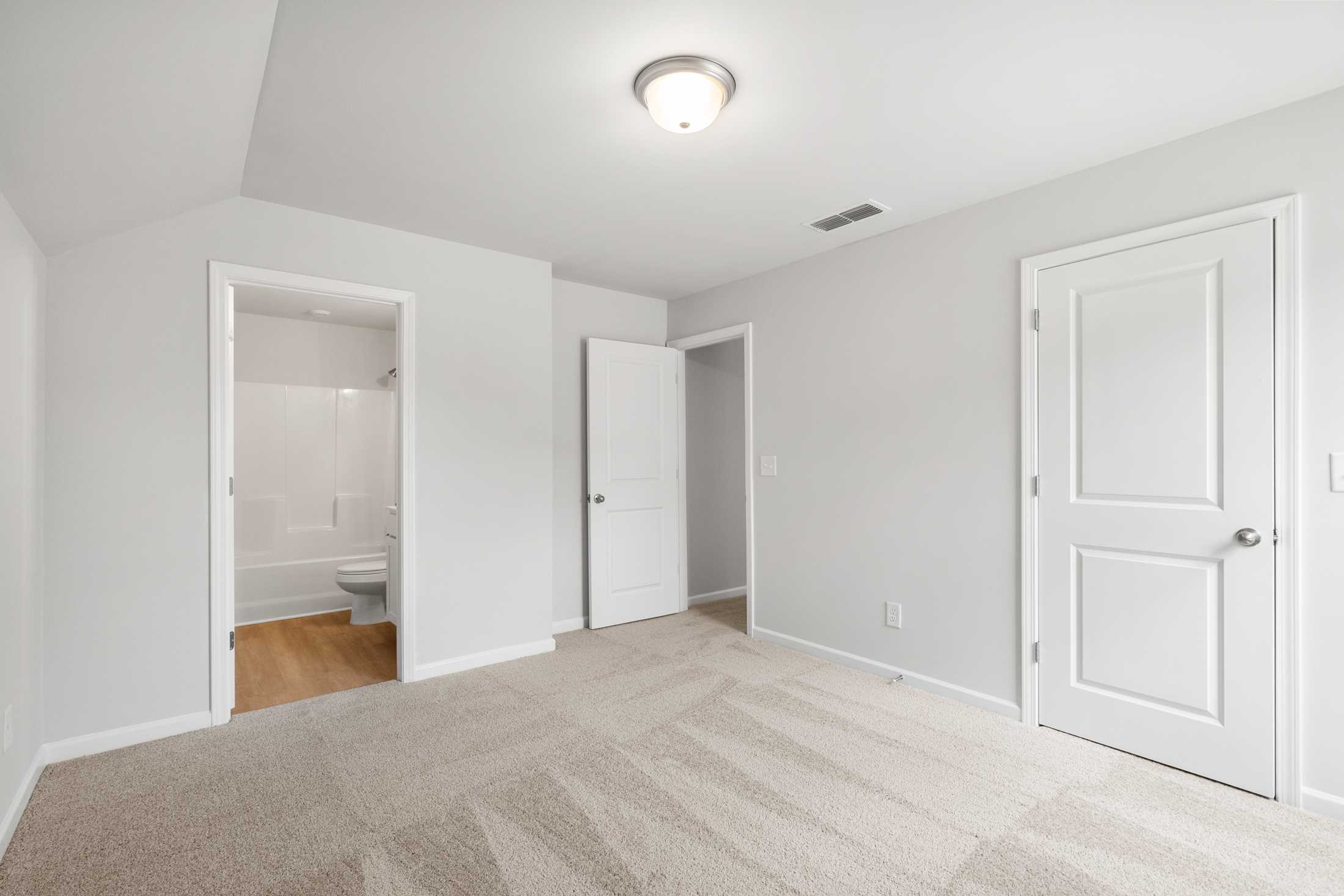 Spacious secondary bedroom in The Ash B featuring gray walls, carpeted floor, and attached bathroom with tub