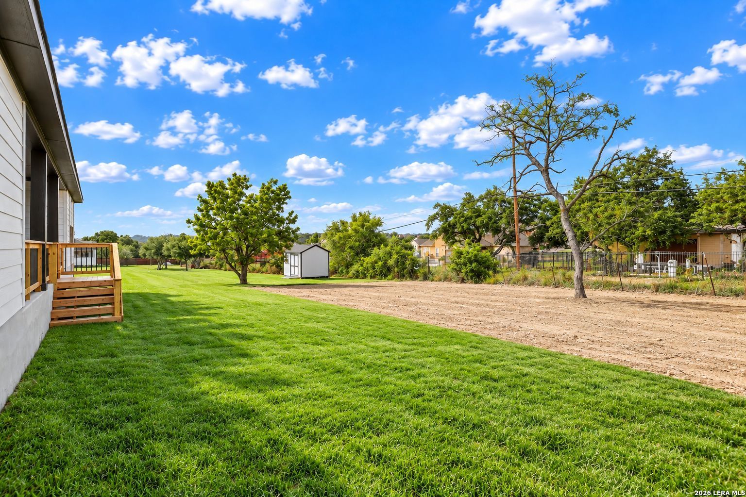 Spacious backyard with green lawn, wooden deck stairs, and mature trees at Davidson Homes The Oxford F in Potranco Oaks, Castroville, TX