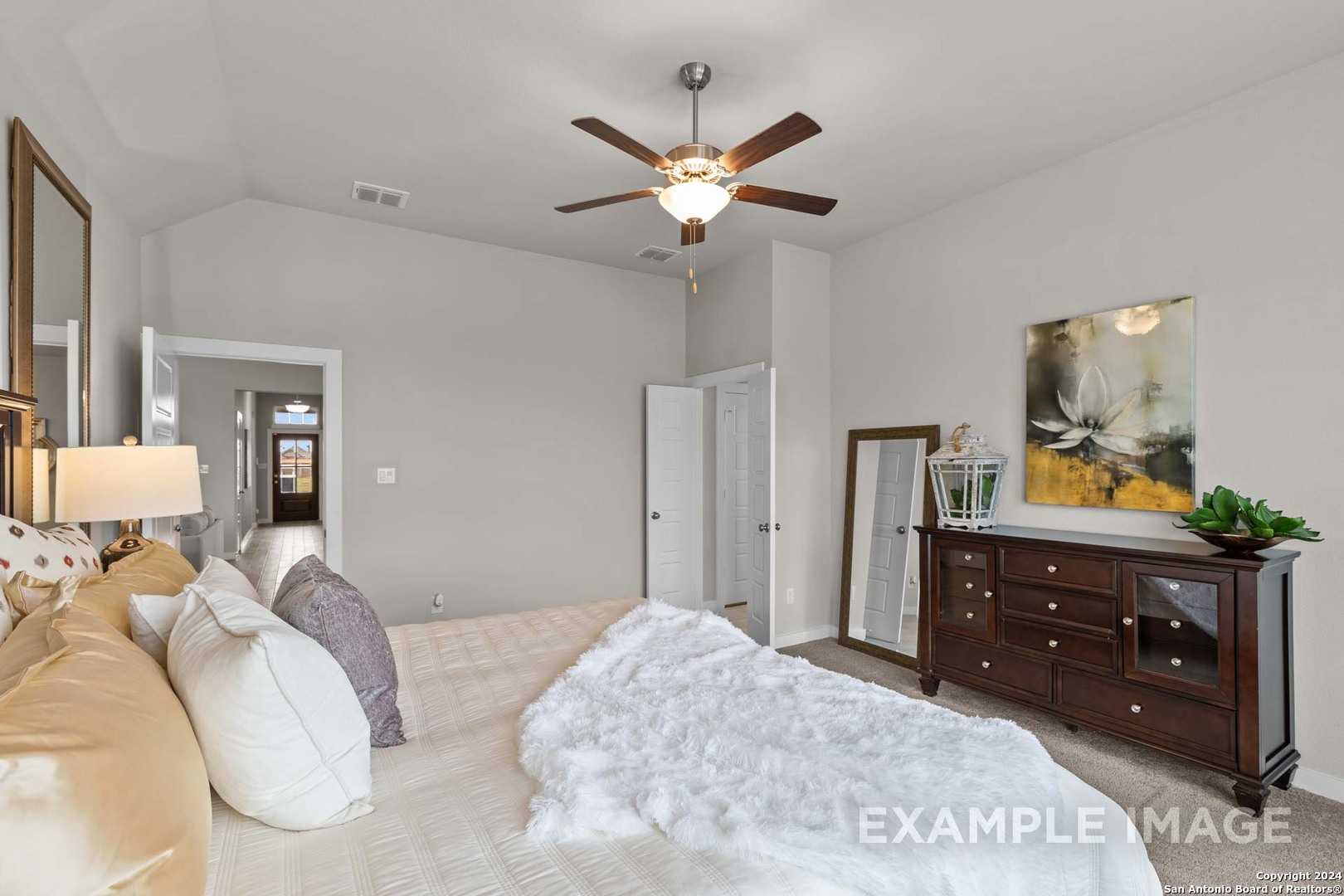 Elegant master bedroom with plush king bed, ceiling fan, wooden dresser, and abstract art in Davidson Homes The Collin B, Seguin, Texas