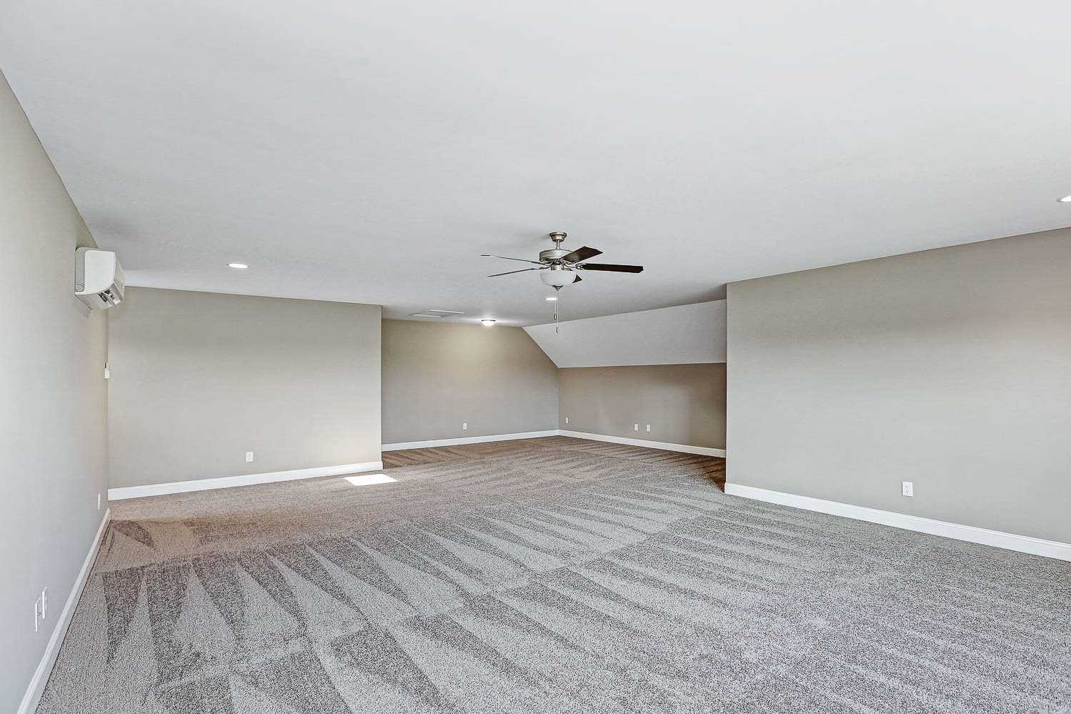 Spacious bonus room in The Montgomery featuring vaulted ceilings, ceiling fan, beige walls, and gray carpet flooring