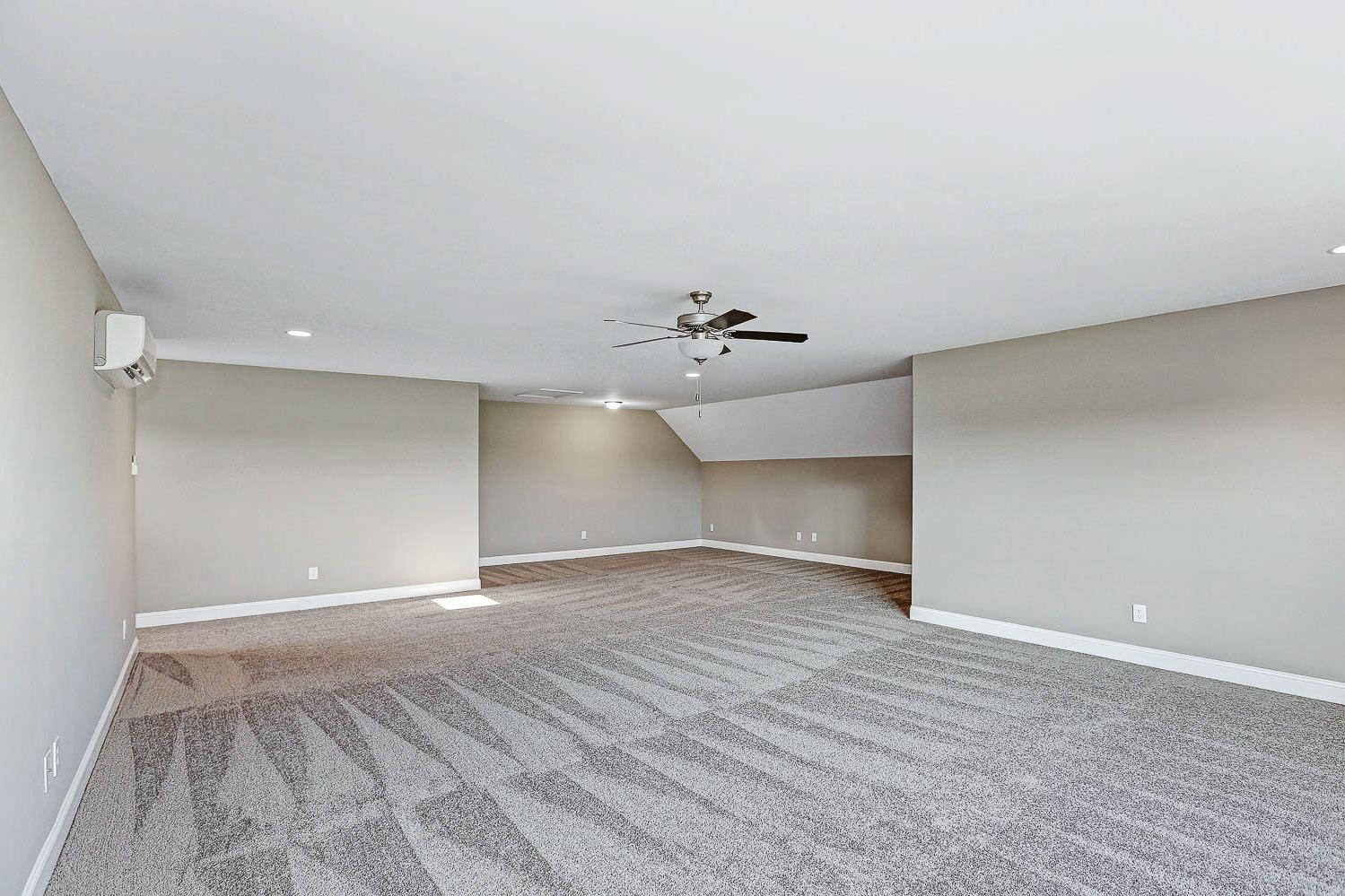 Spacious bonus room in The Montgomery featuring vaulted ceilings, ceiling fan, beige walls, and gray carpet flooring