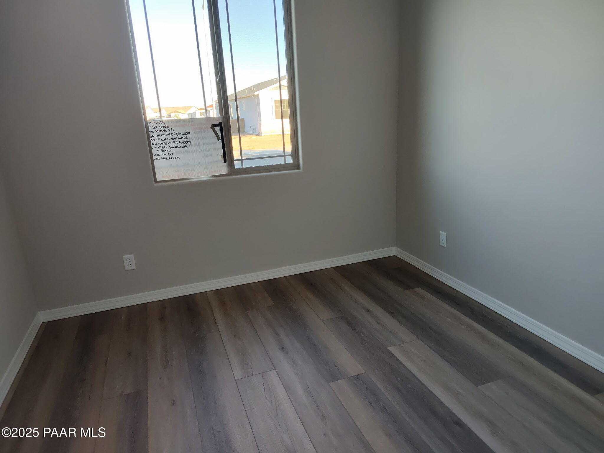 Spacious empty bedroom with neutral beige walls, laminate wood floors, and large window in Davidson Homes The Frontier C, Prescott Valley, Arizona